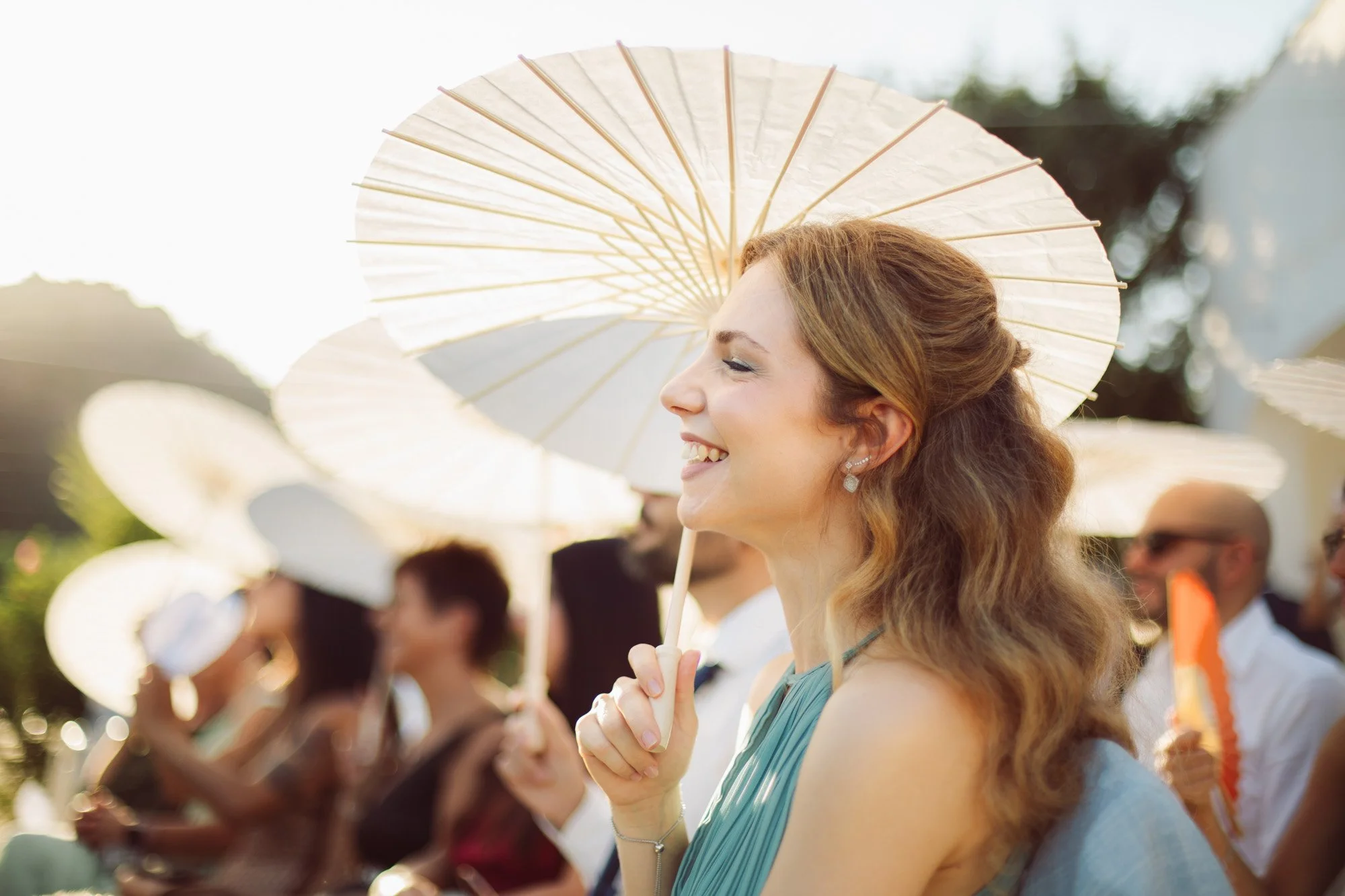 Un'invitata sorridente con un elegante ombrellino parasole bianco durante la cerimonia di matrimonio all'aperto.