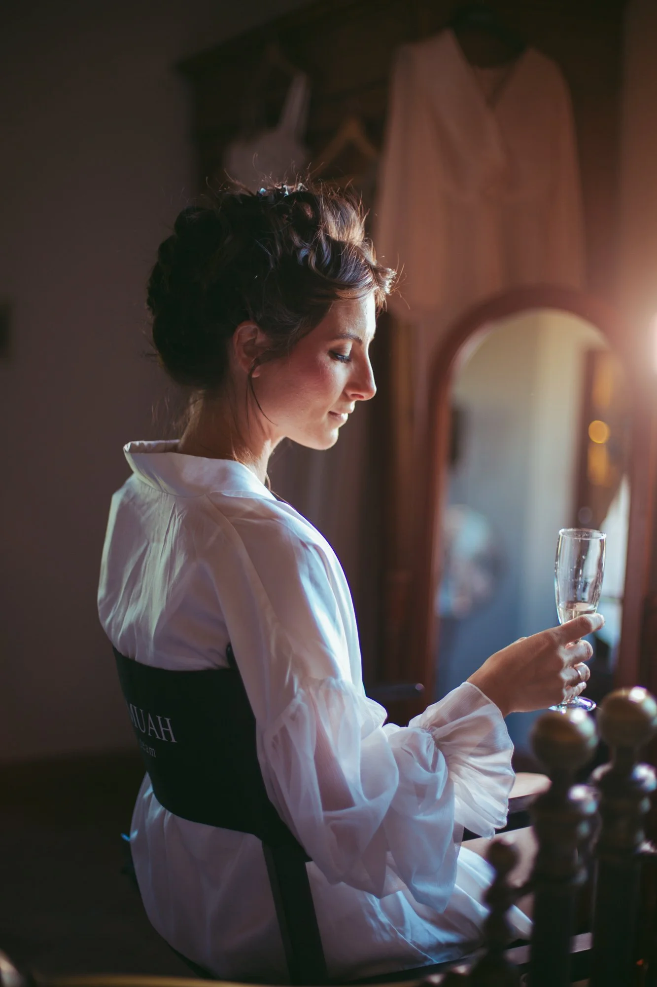 Ritratto di profilo della sposa in vestaglia bianca con un calice di champagne in mano