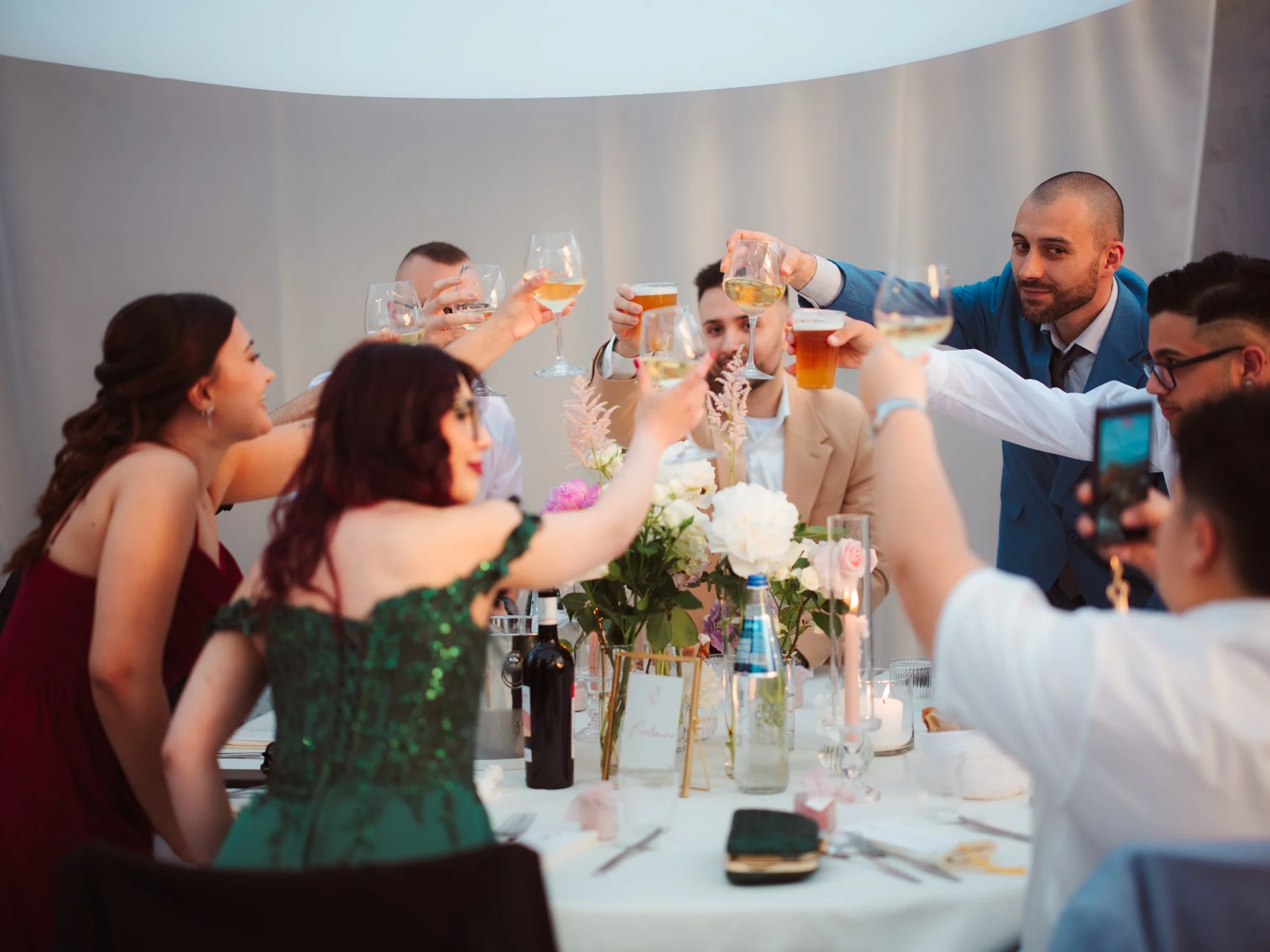 Gli invitati al matrimonio sollevano i calici di vino e birra al centro del tavolo per un brindisi conviviale