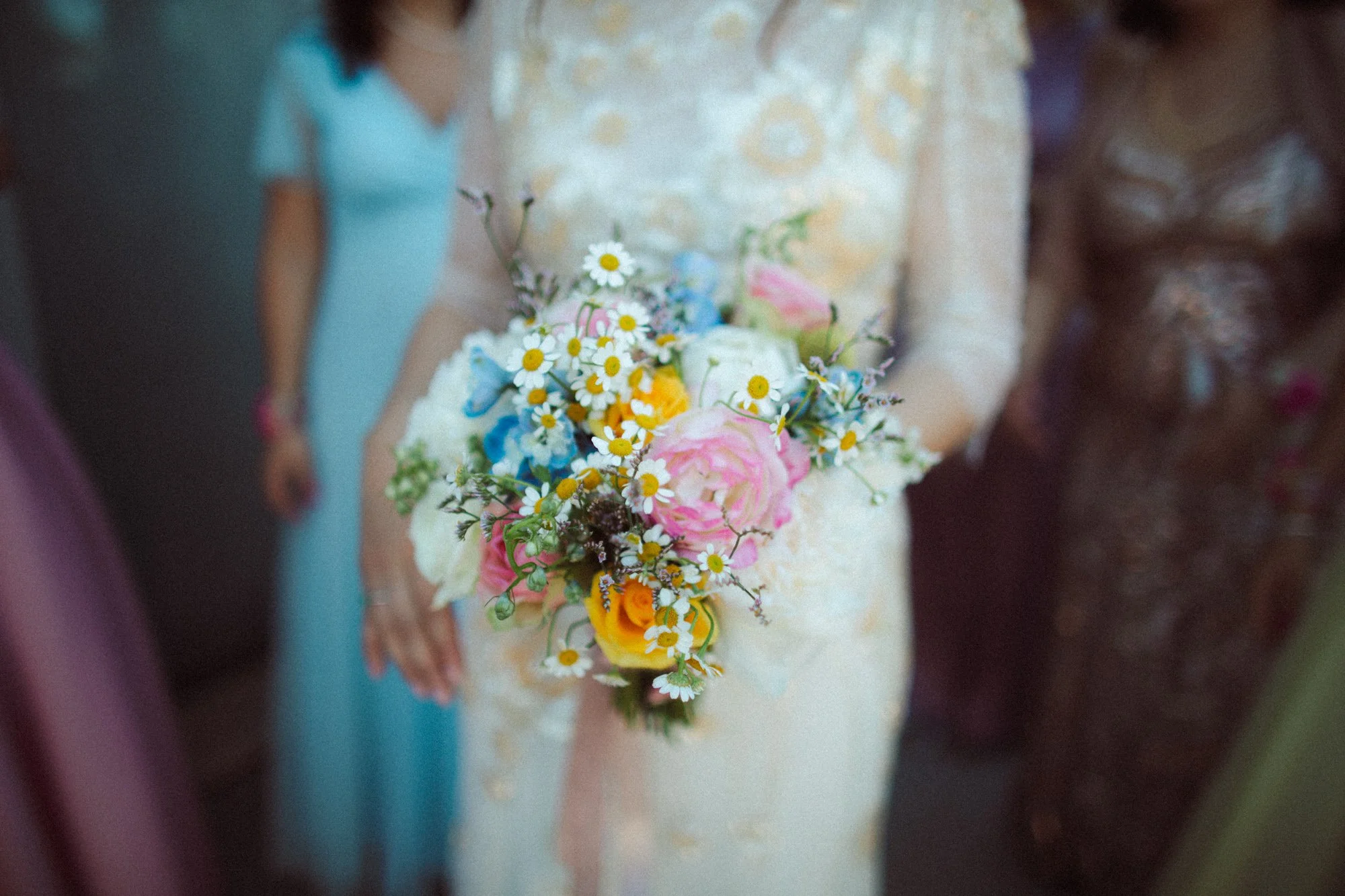 La sposa tiene in mano il bouquet di fiori di campo colorati con le invitate e le damigelle attorno