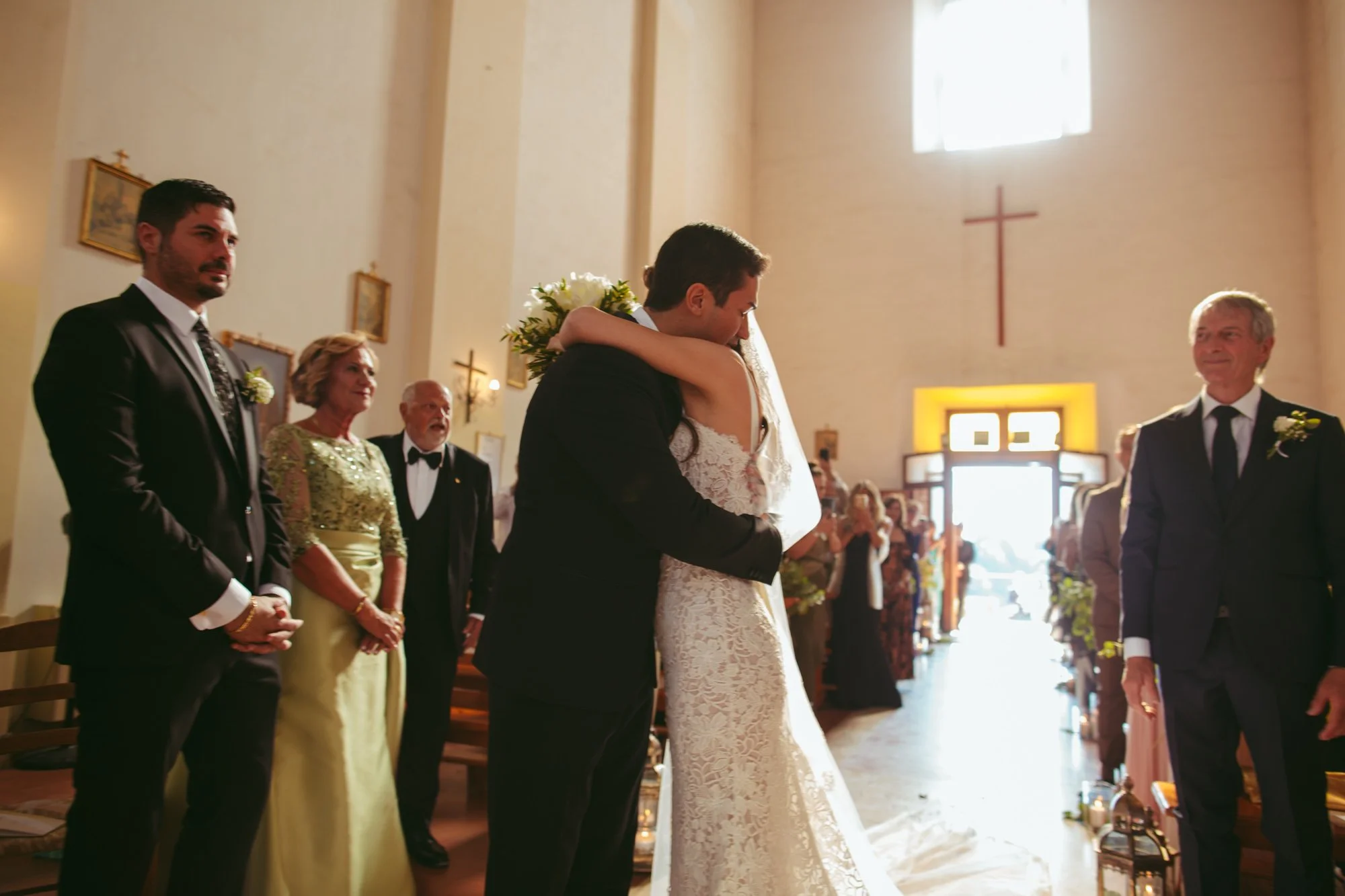 Lo sposo abbraccia la sposa all'arrivo all'altare davanti ai testimoni e ai genitori