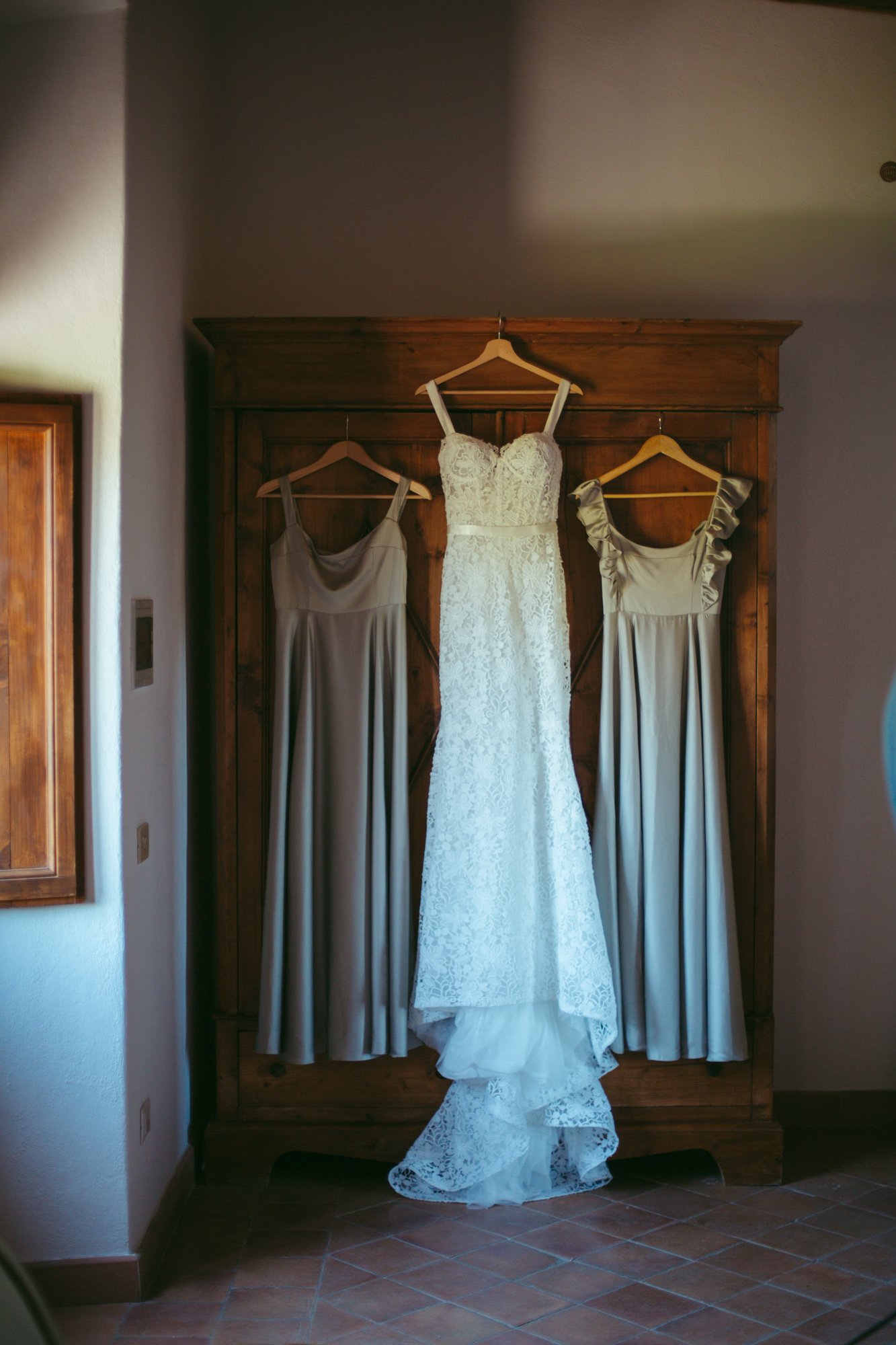 Abito da sposa in pizzo e abiti delle dame d'onore appesi all'armadio in stile rustico a Borgo di Tragliata