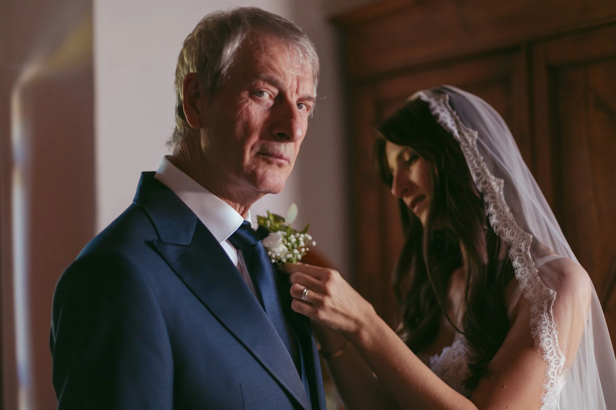La sposa sistema la bottoniera di fiori bianchi sul revere della giacca del padre