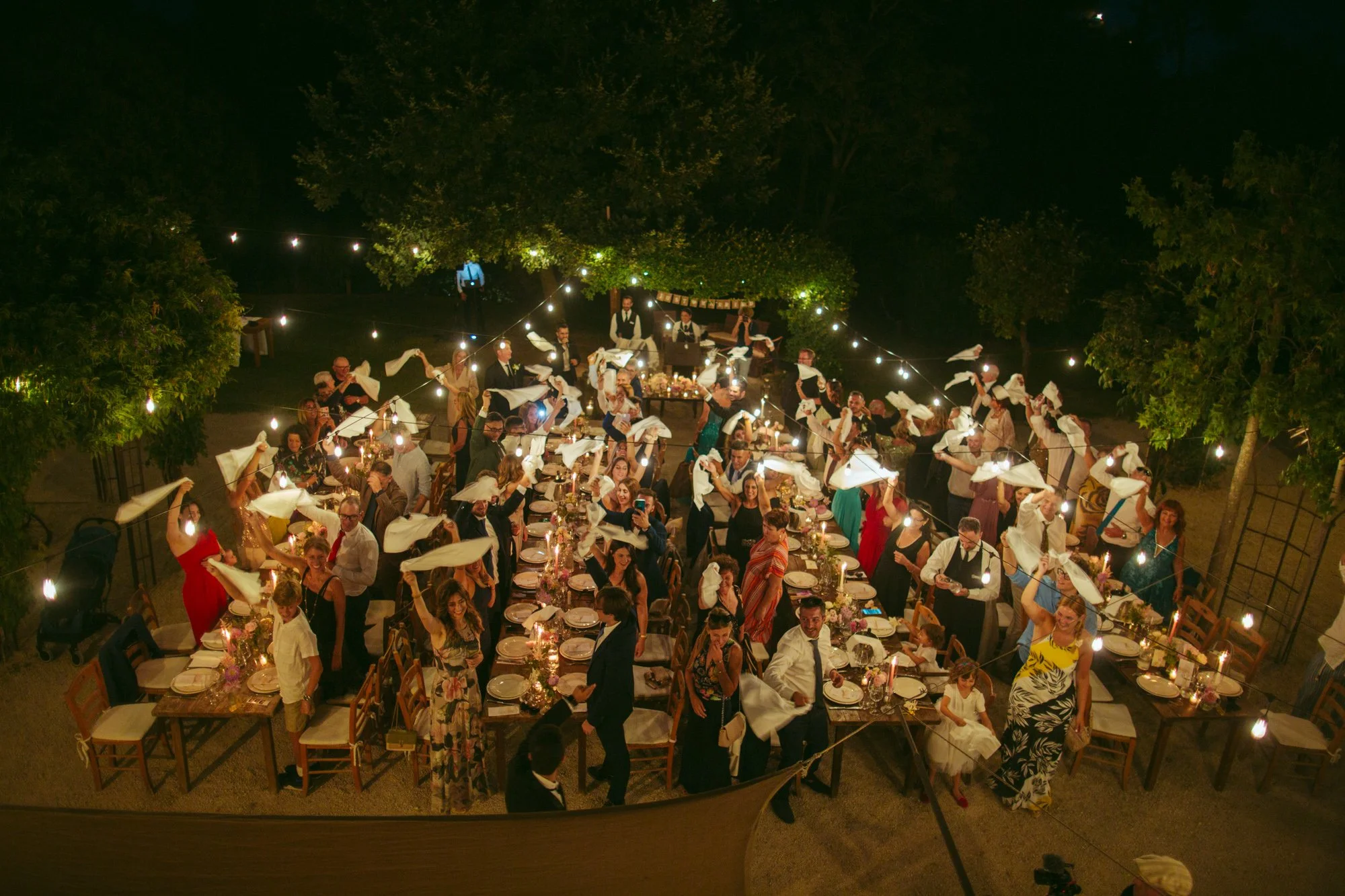 Vista dall'alto degli invitati che festeggiano sventolando i tovaglioli durante la cena di matrimonio al Borgo di Tragliata