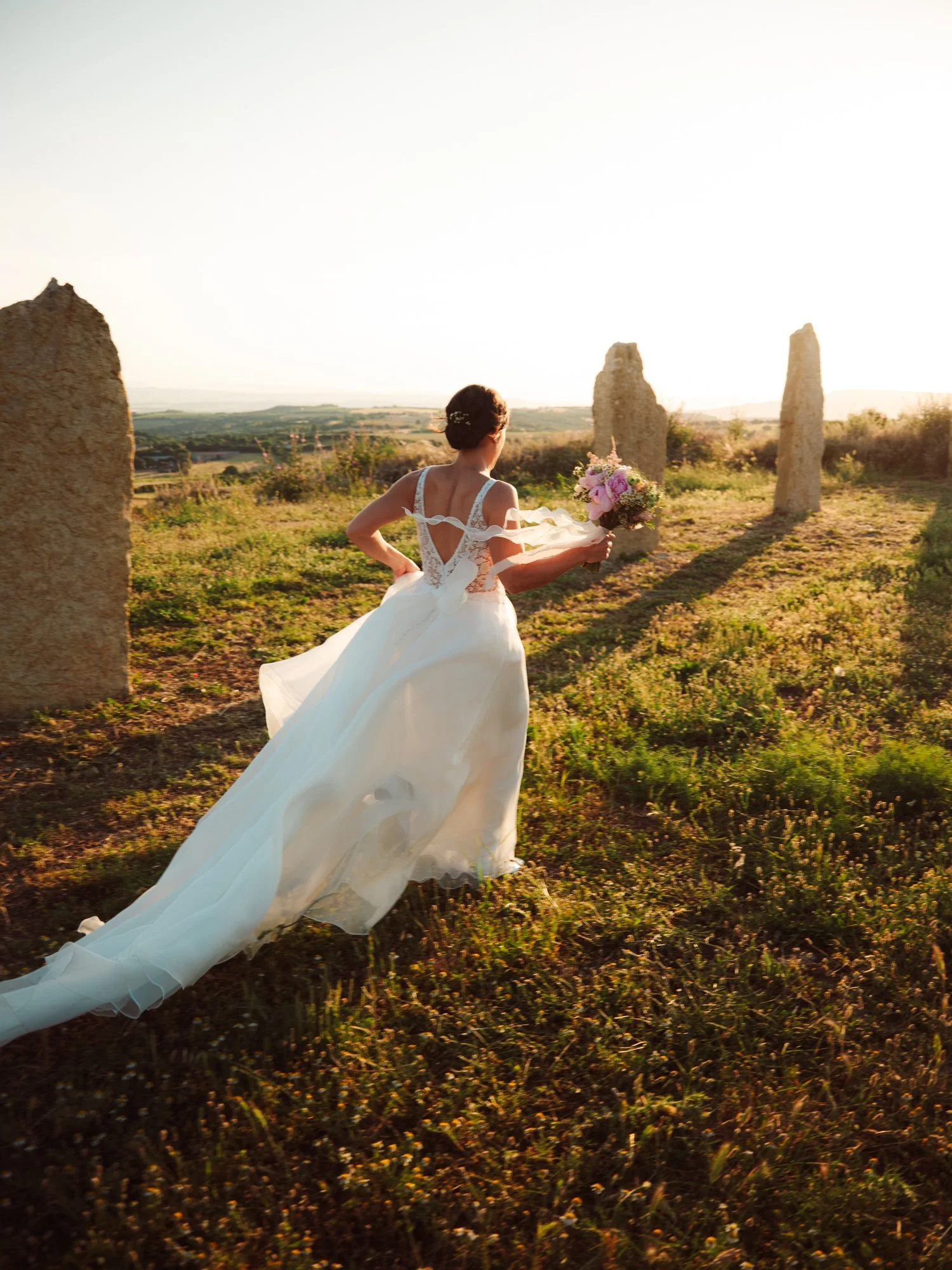 Sposa in movimento nei campi sardi con lungo strascico al tramonto
