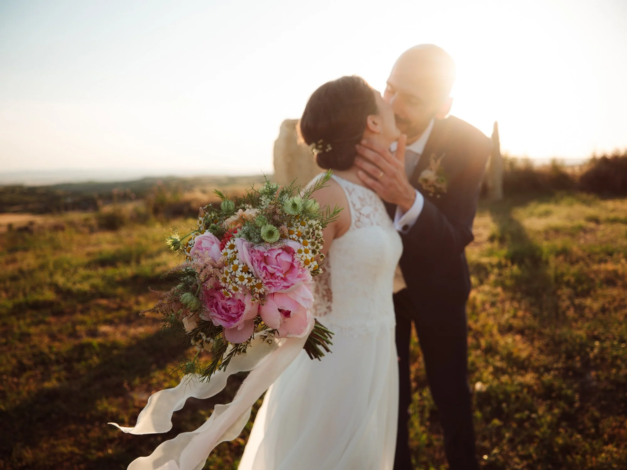 Dettaglio del bouquet da sposa in primo piano con bacio degli sposi in secondo piano