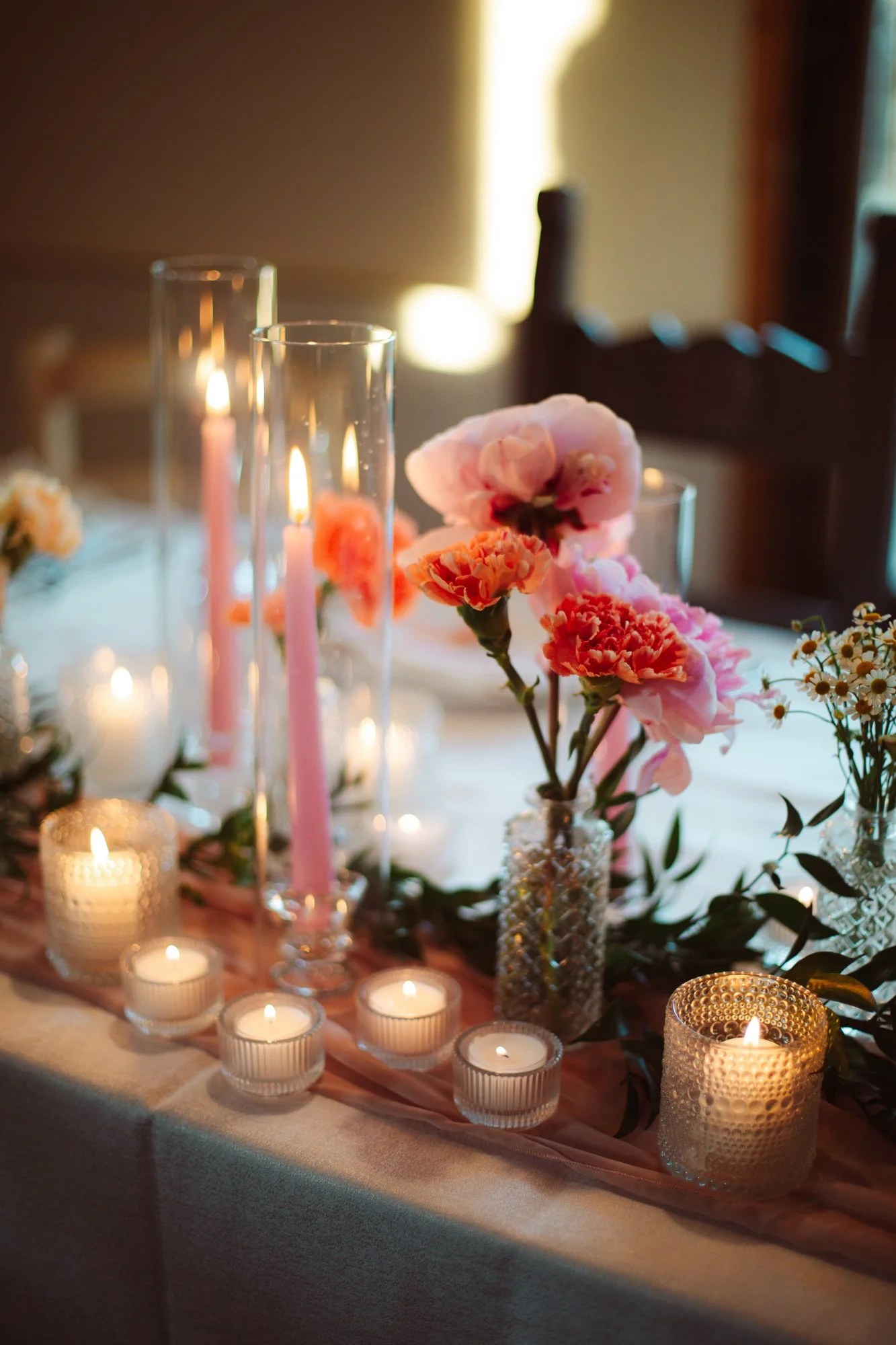 Centrotavola elegante con candele rosa in tubi di vetro, piccoli vasi floreali e runner su tavola nuziale