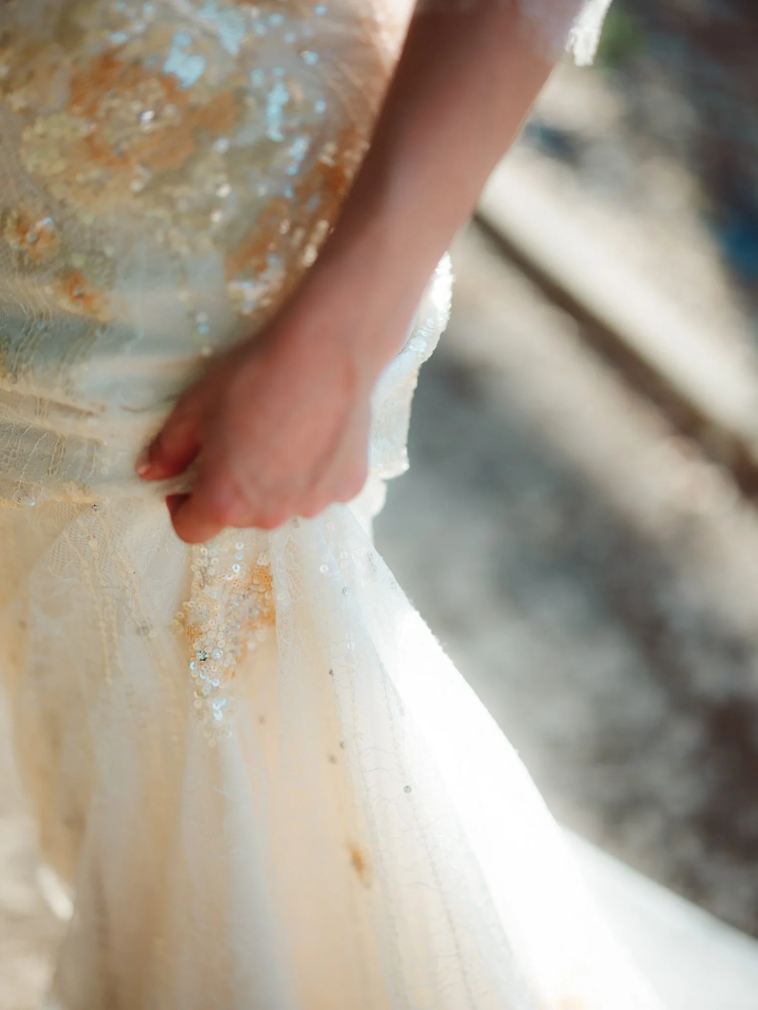 Mano della sposa che tiene il tessuto pregiato del vestito mettendo in mostra le ricche lavorazioni in paillettes e pizzo