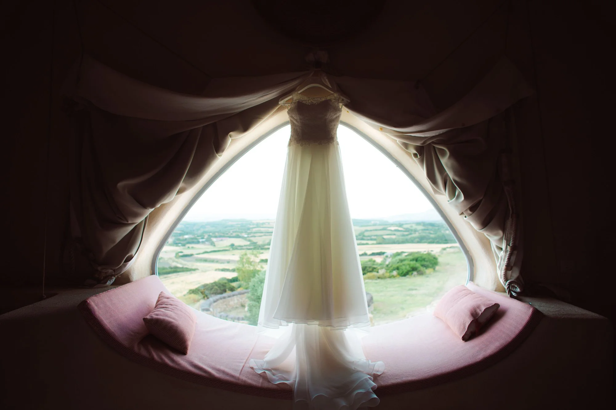 Abito da sposa appeso a una finestra panoramica sul paesaggio durante la preparazione del matrimonio in Sardegna