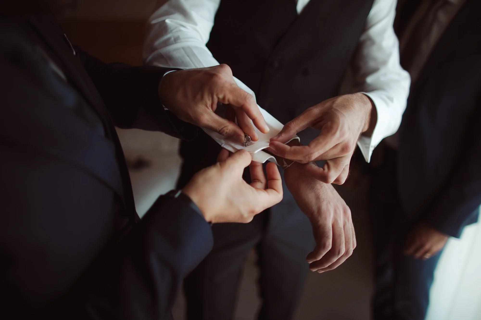 Primo piano delle mani di un testimone che aiuta lo sposo a chiudere i gemelli della camicia da cerimonia