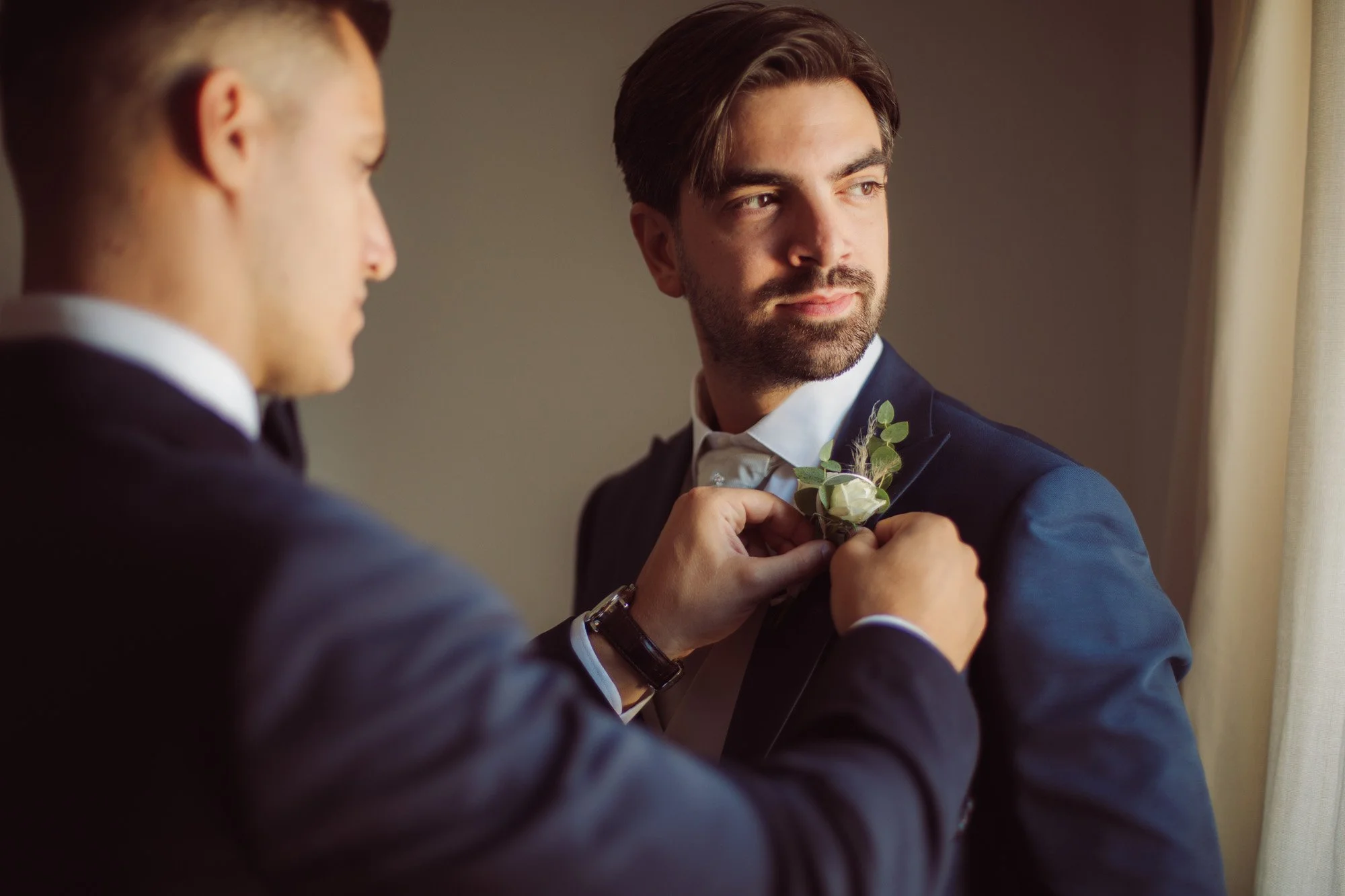 Il testimone appunta la boutonnière floreale sul risvolto della giacca dello sposo durante i preparativi.
