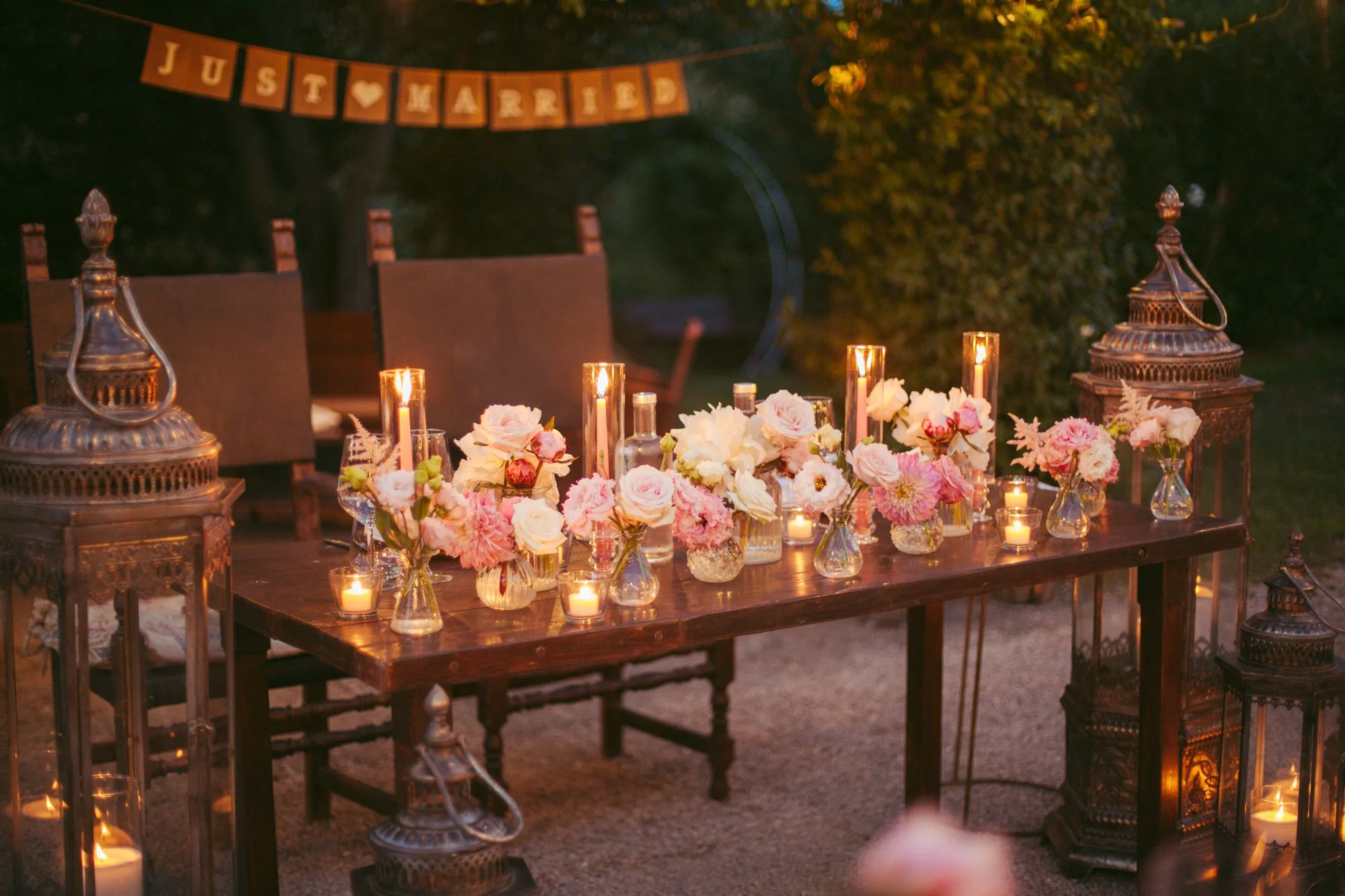 Allestimento del tavolo degli sposi con composizioni floreali rosa, candele accese e lanterne vintage al Borgo di Tragliata