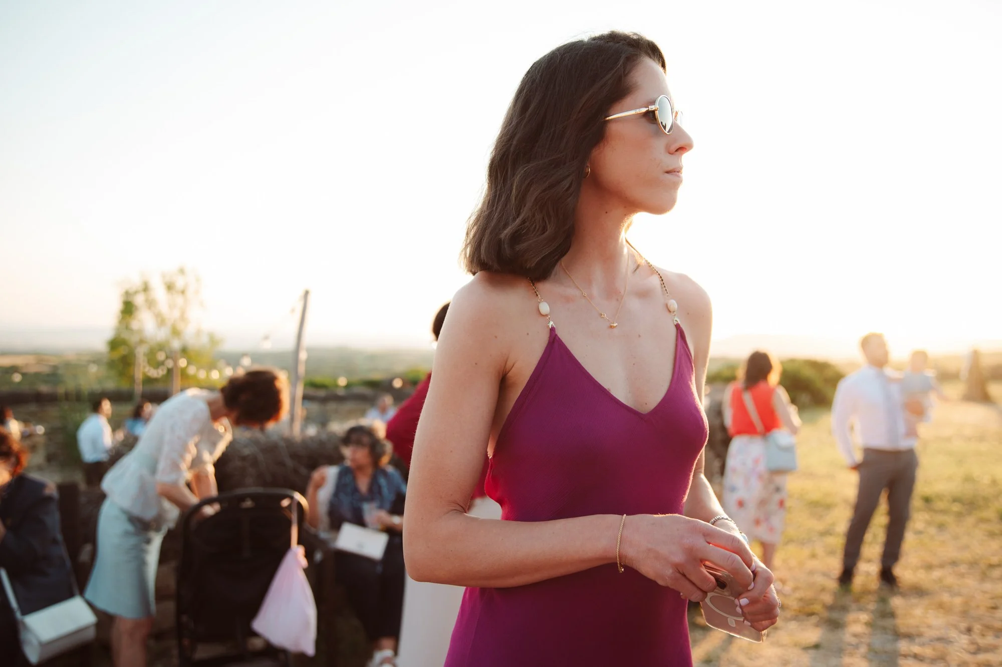 Invitata a un matrimonio all'aperto in Sardegna con abito viola fucsia e occhiali da sole al tramonto
