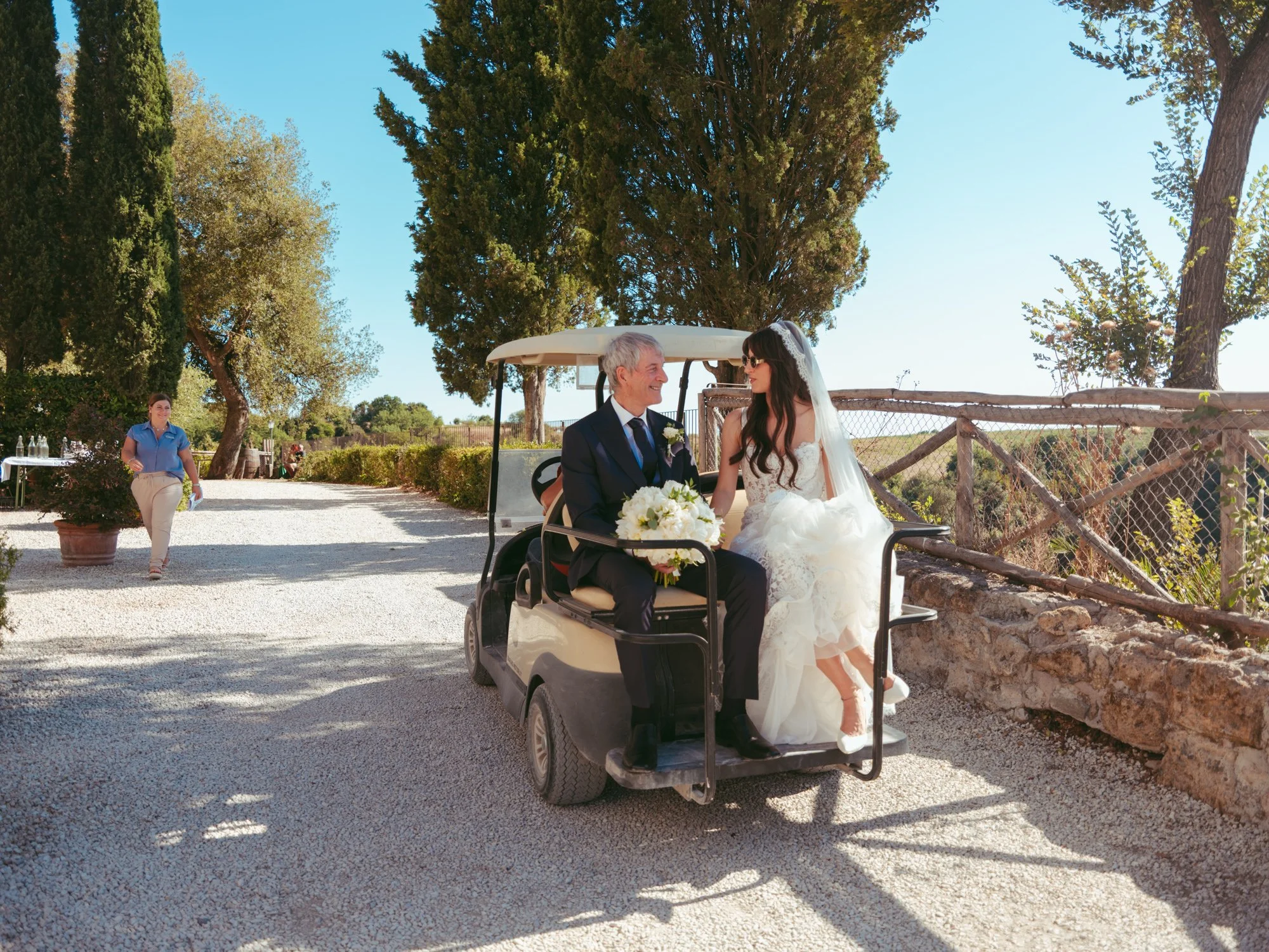 La sposa e il padre seduti a bordo del golf cart mentre si dirigono verso il luogo delle nozze