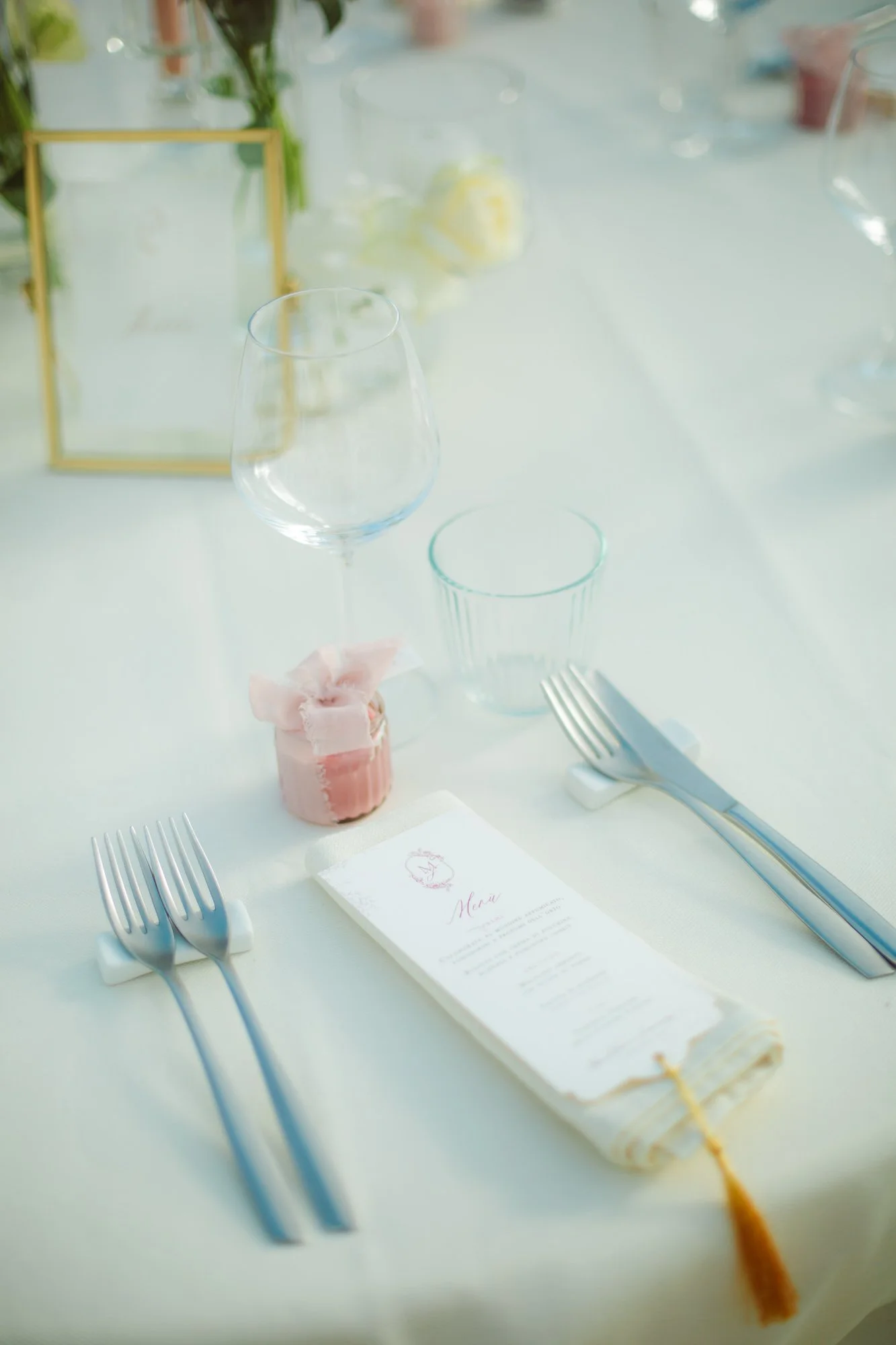 Dettaglio elegante della mise en place con posate moderne, calici in vetro, menu cartaceo e bomboniera rosa