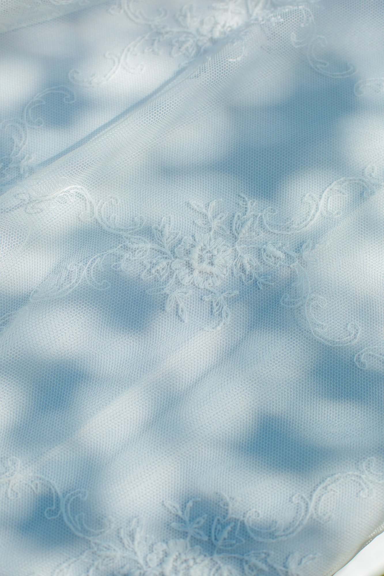 Dettaglio ravvicinato del raffinato pizzo ricamato dell'abito da sposa accarezzato da ombre e luci naturali