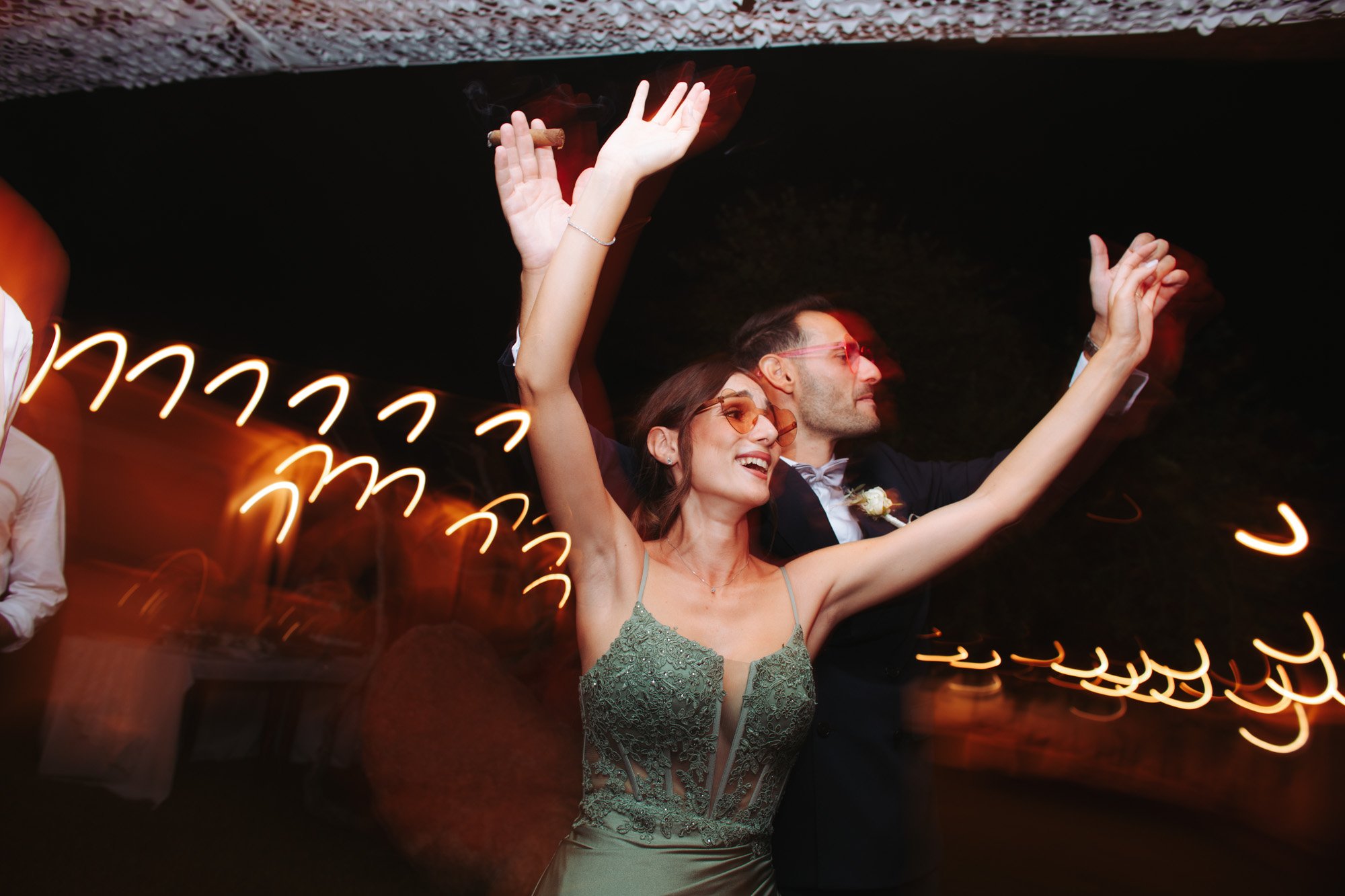 Inviti e sposi con le braccia alzate festeggiano in pista durante la festa serale del matrimonio.