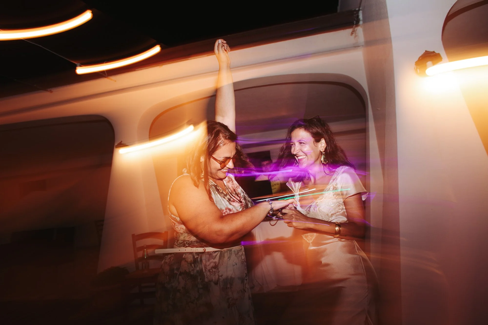 Due invitate scatenate sulla pista da ballo durante il ricevimento serale del matrimonio con luci calde e suggestive.
