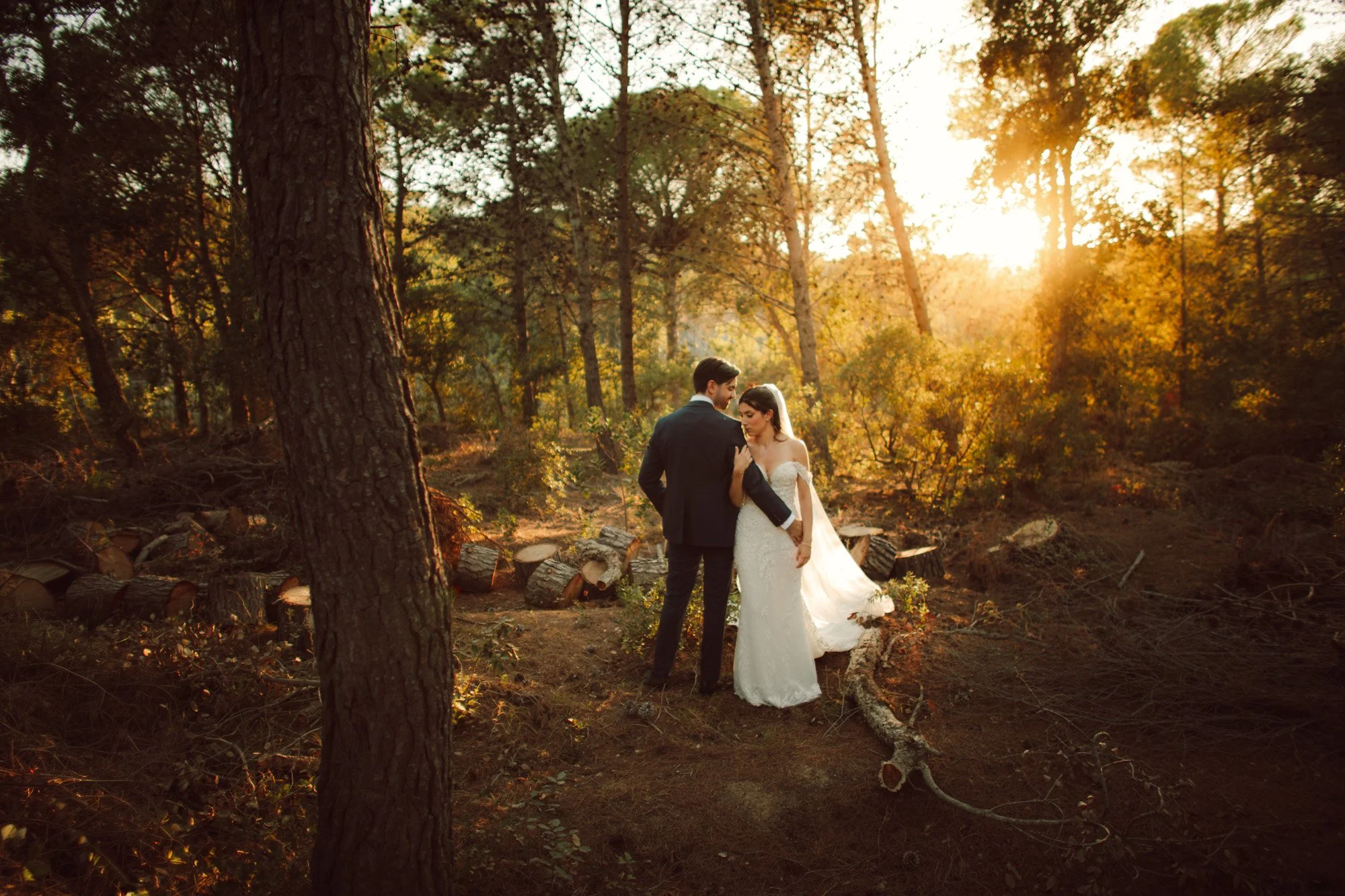 Sposi abbracciati in un bosco illuminato da una calda luce cinematografica al tramonto durante il loro matrimonio di lusso in Italia.