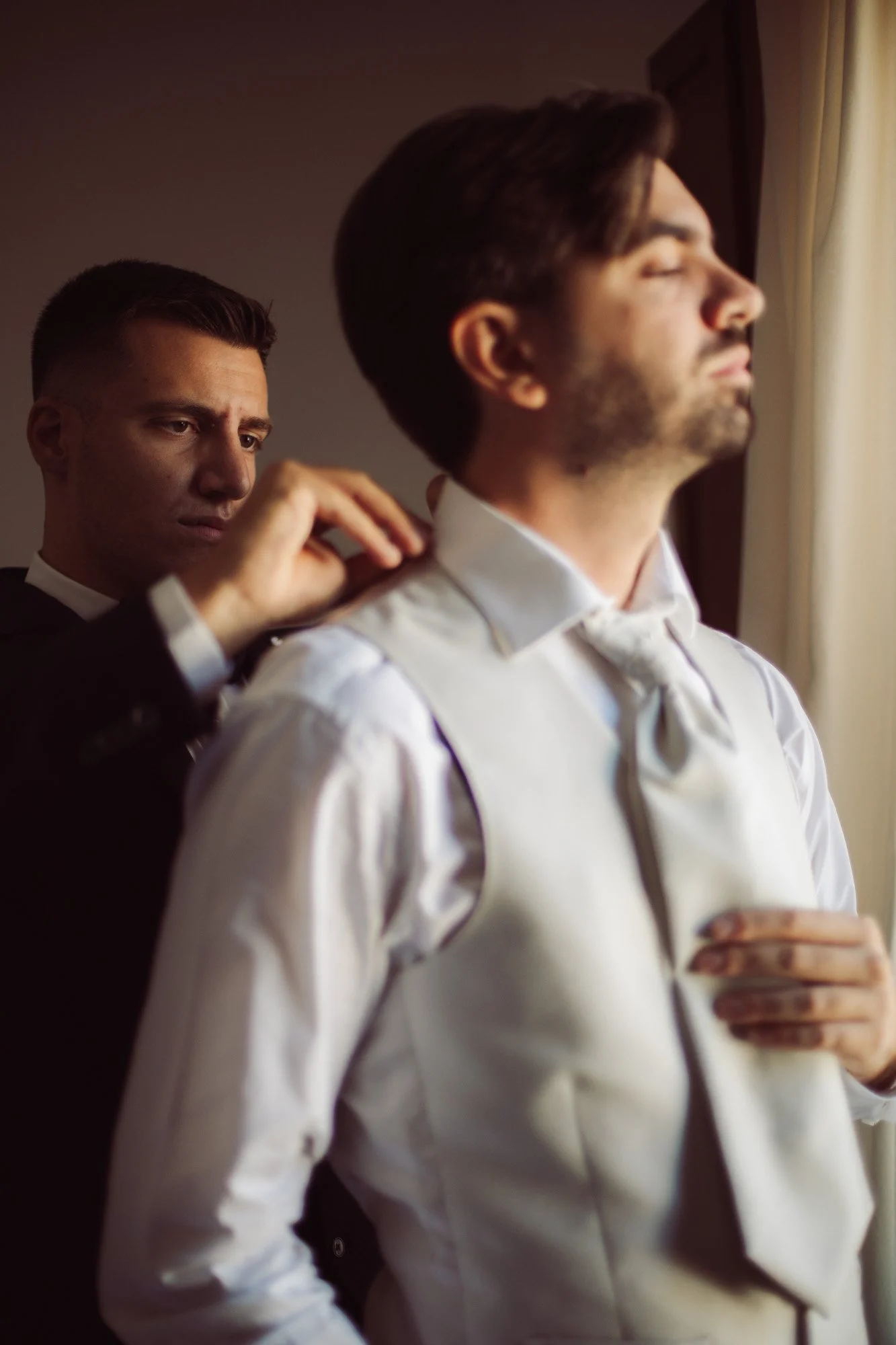 Lo sposo si aggiusta la cravatta e il colletto della camicia alla luce naturale accanto alla finestra