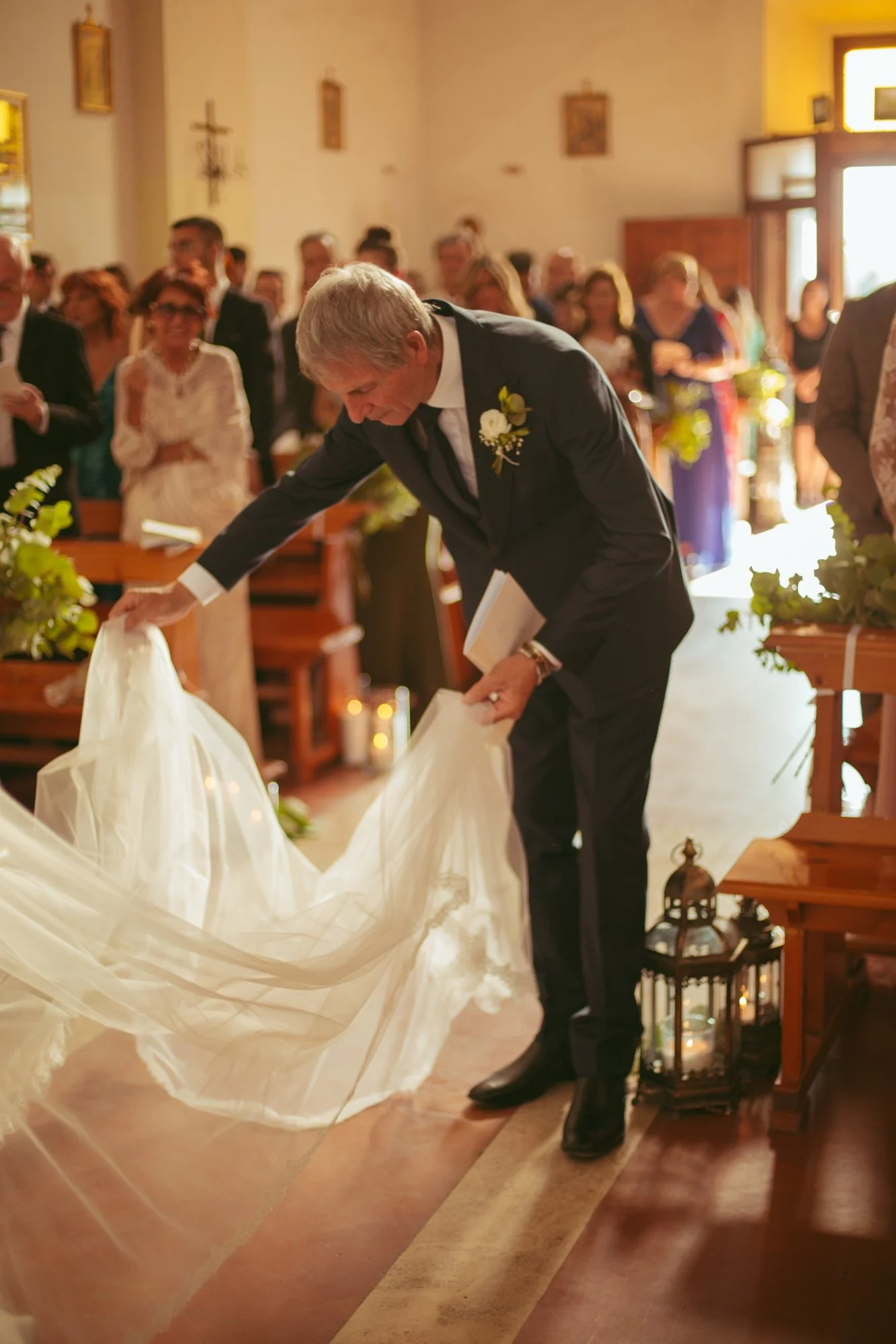 Il padre della sposa si china per sistemare il lungo velo in pizzo prima di percorrere la navata della chiesa