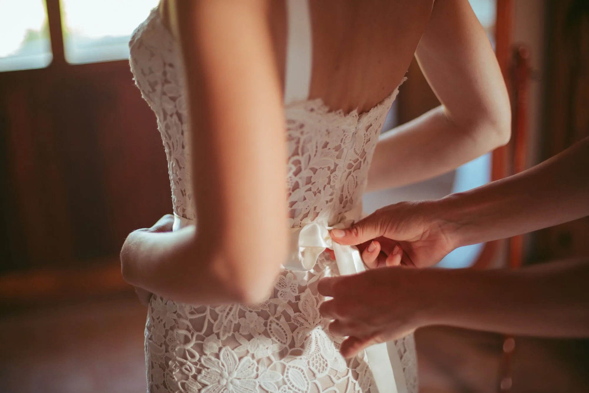 Dettaglio del fiocco in raso allacciato in vita sull'abito da sposa in pizzo