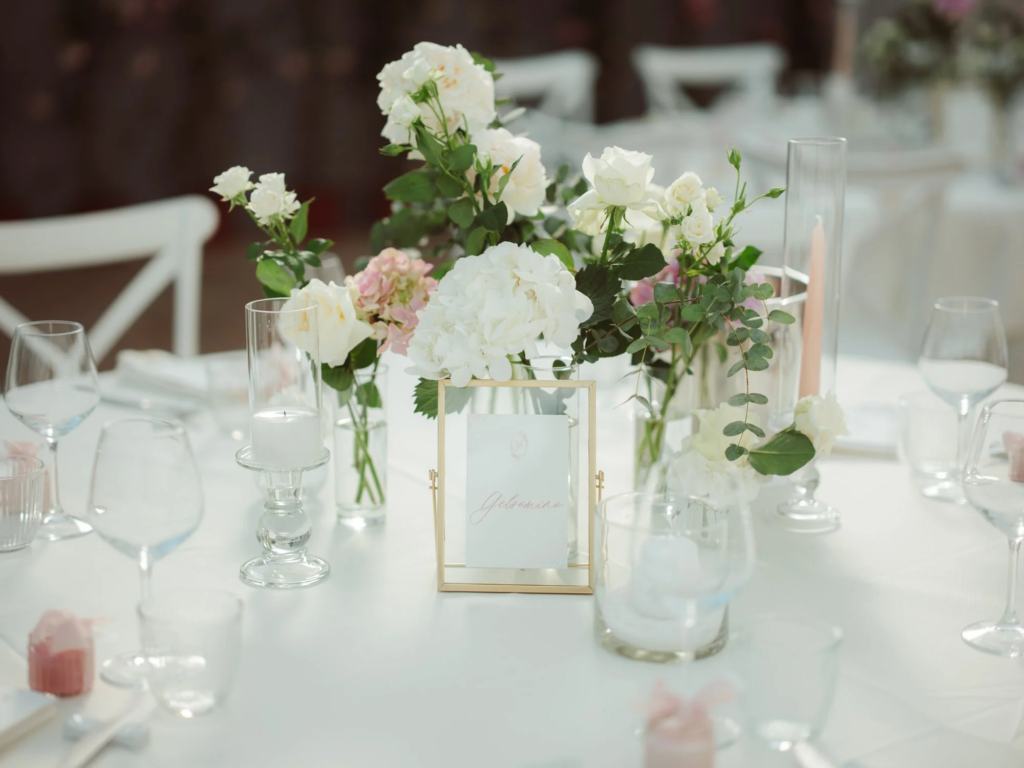 Centrotavola con ortensie e rose bianche affiancato dal segnatavolo in cornice dorata recante la scritta Gelsomino