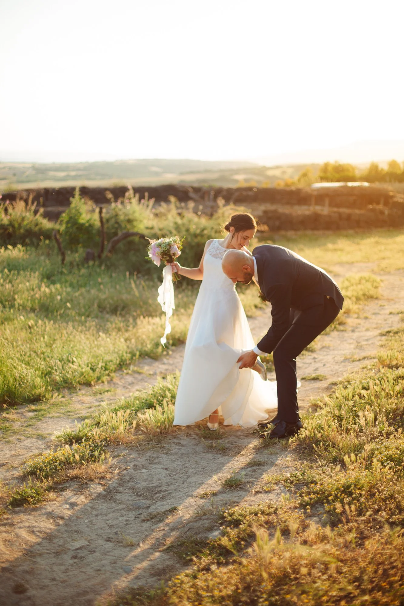 Lo sposo aiuta la sposa con il vestito durante la passeggiata al tramonto