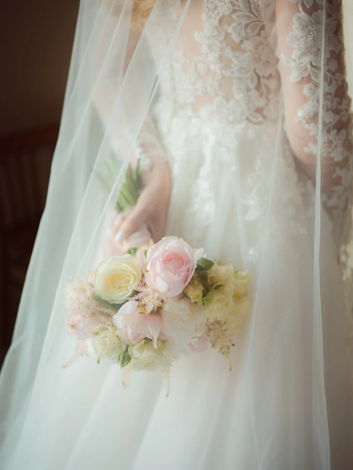 Un bouquet di fiori bianchi e rosa retto da una mano, visto attraverso il velo di una sposa, con dettagli dell'abito di nozze.