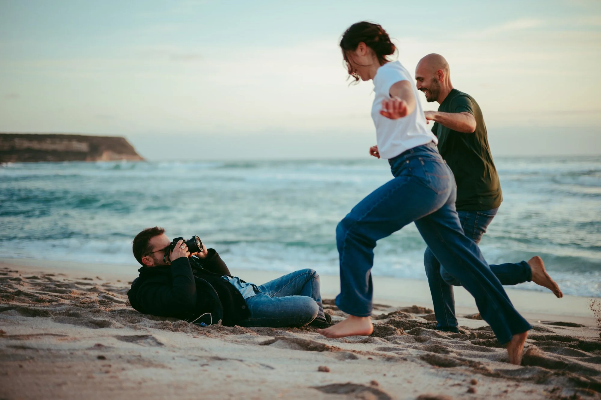 l fotografo Marco Ciampelli steso sulla sabbia mentre fotografa una coppia che corre sulla spiaggia al tramonto