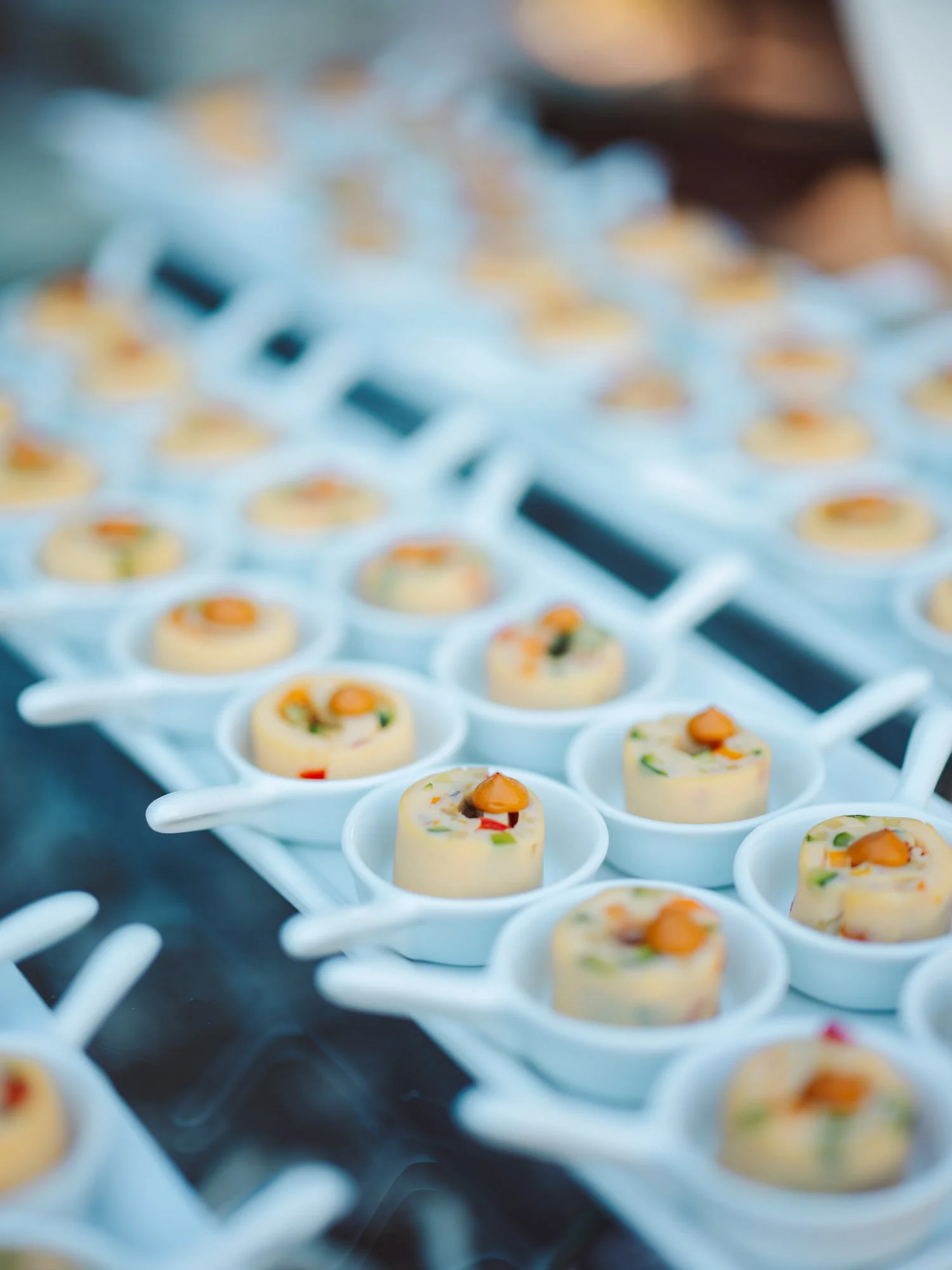 Elegante alzata con monoporzioni di finger food salato disposte su cucchiai bianchi per l'aperitivo nuziale