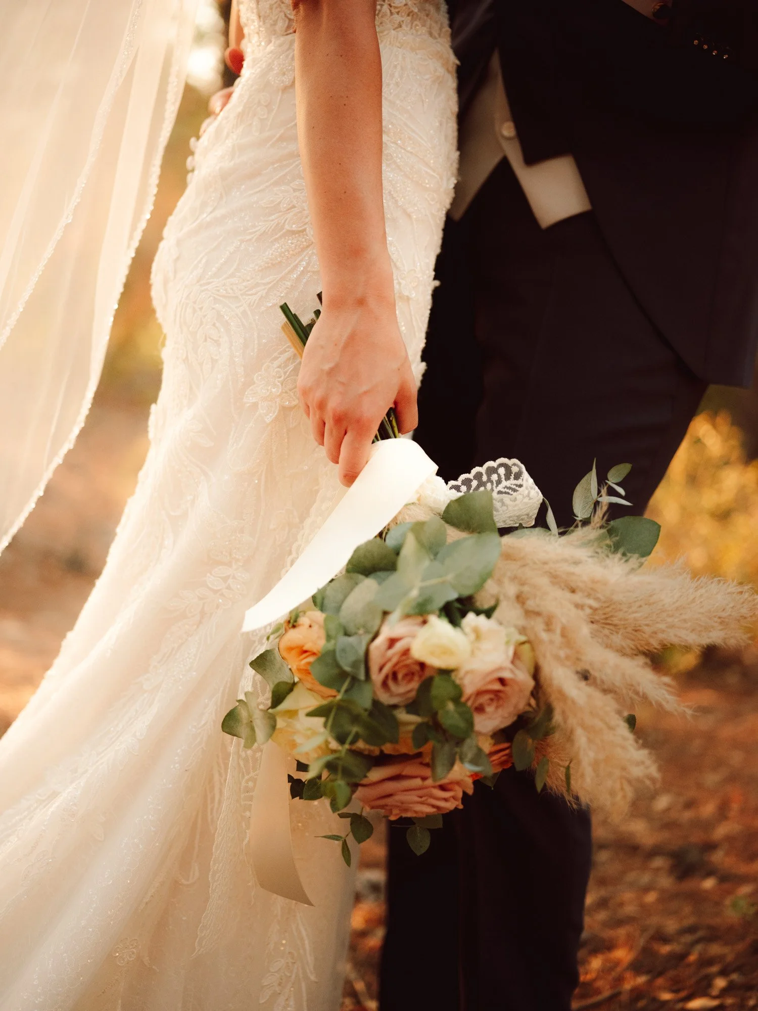 Primo piano del bouquet di rose e del vestito in pizzo della sposa accanto all'abito dello sposo