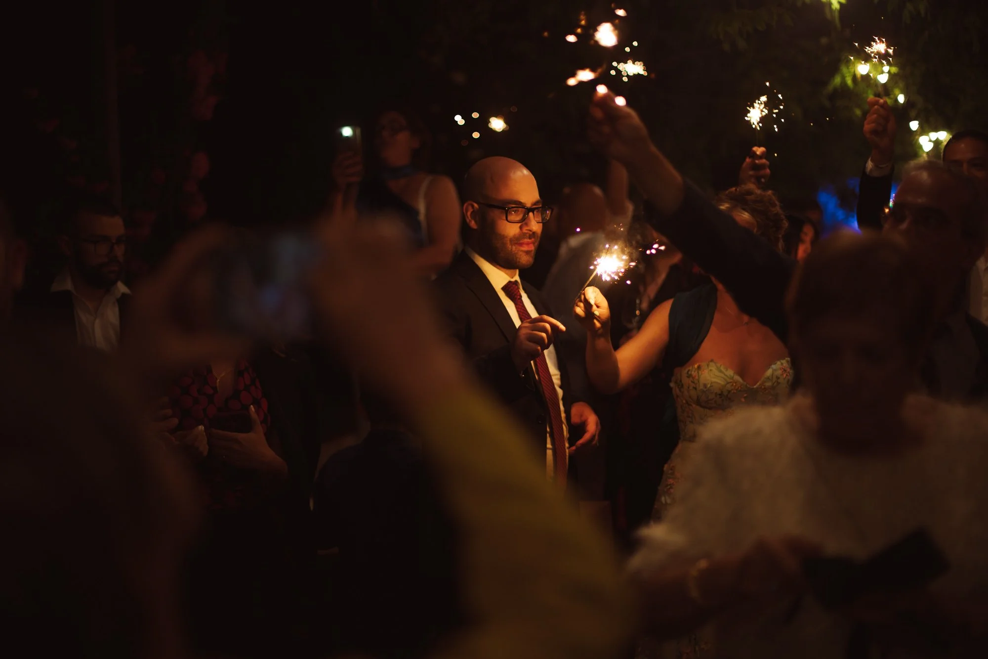 Invitato con occhiali sorride tenendo in mano una stellina sparkler accesa durante la festa di notte