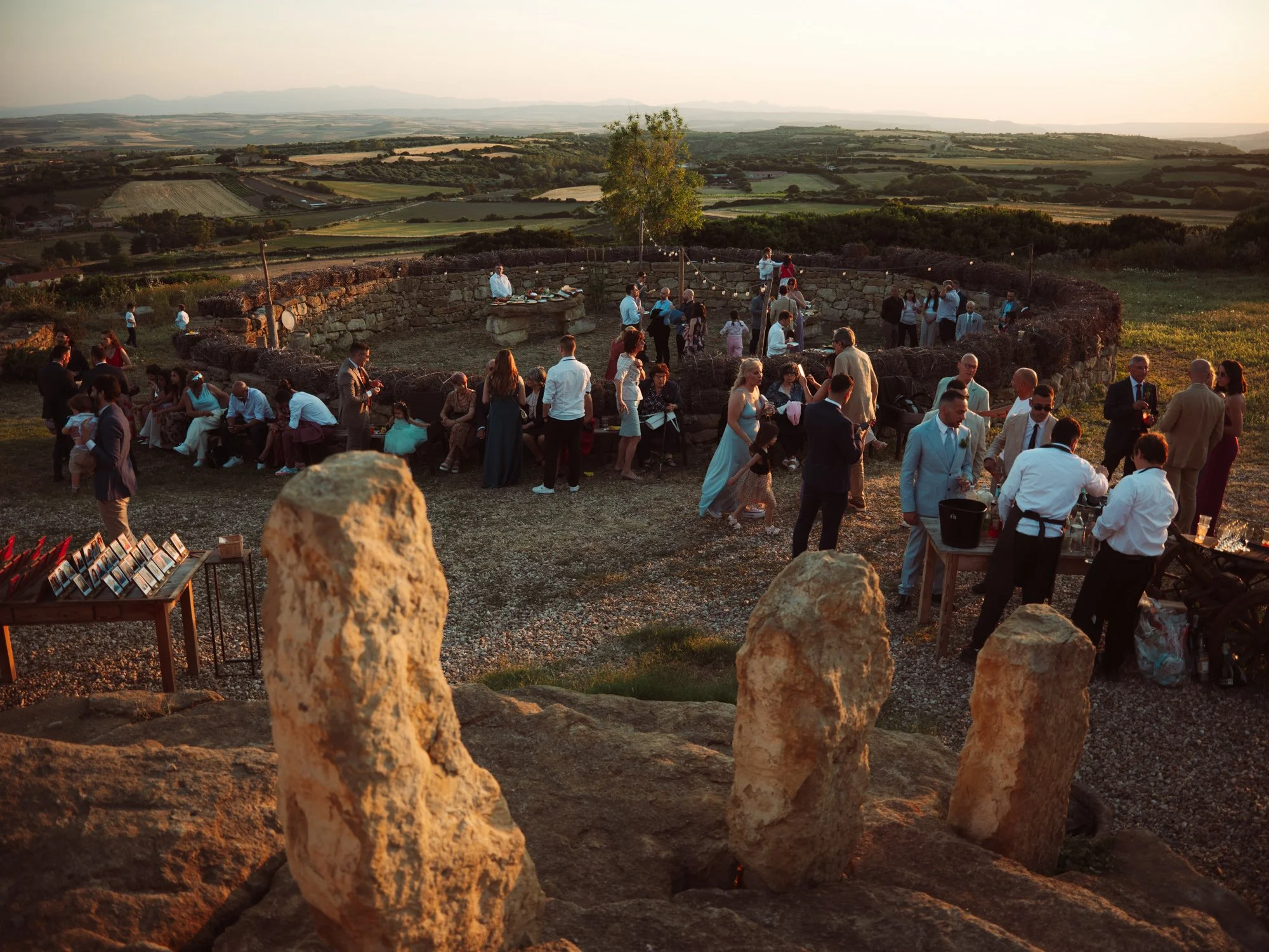 Vista panoramica dall'alto dell'aperitivo di nozze all'aperto al tramonto tra roccie e menhir nella campagna sarda
