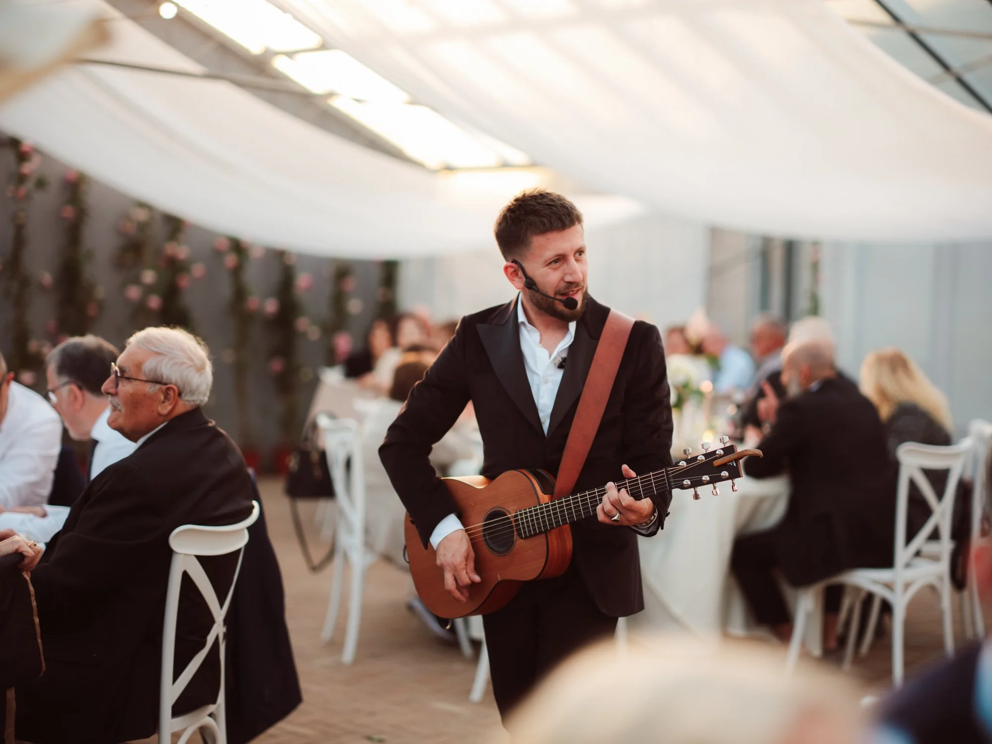 Un musicista con chitarra acustica e archetto microfono suona e canta camminando tra i tavoli degli ospiti
