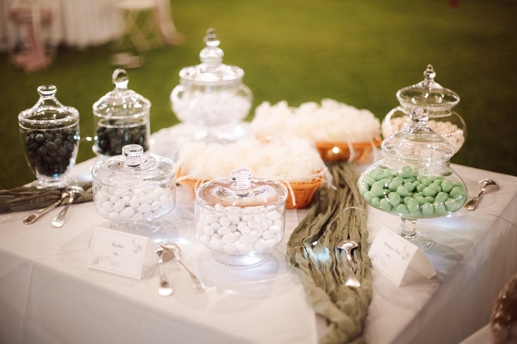 Elegante angolo confettata all'aperto con barattoli di vetro colmi di confetti bianchi e verdi e dettagli curati