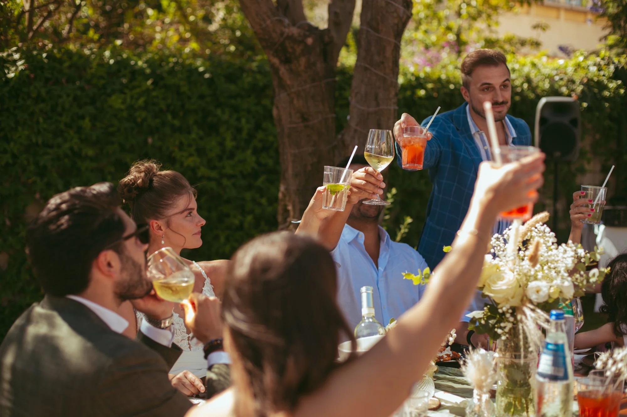 Invitati al matrimonio che alzano calici di vino e bicchieri di cocktail per un brindisi corale intorno al tavolo decorato