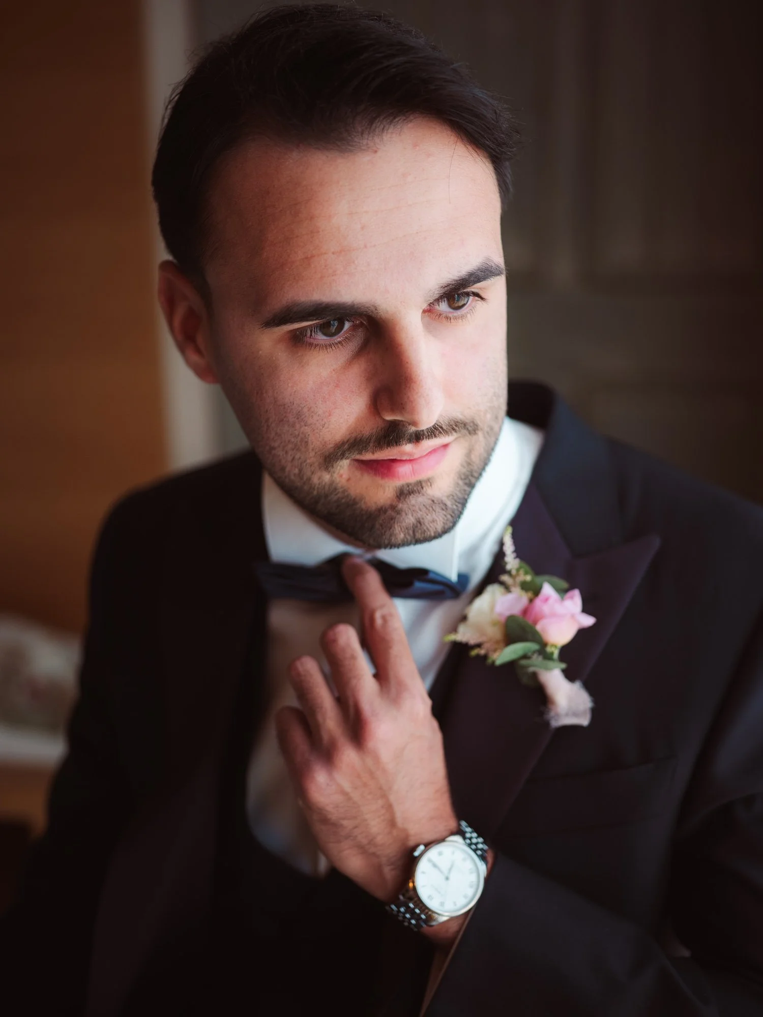 Primo piano dello sposo elegante in giacca scura con bottoniera mentre si aggiusta il papillon al collo