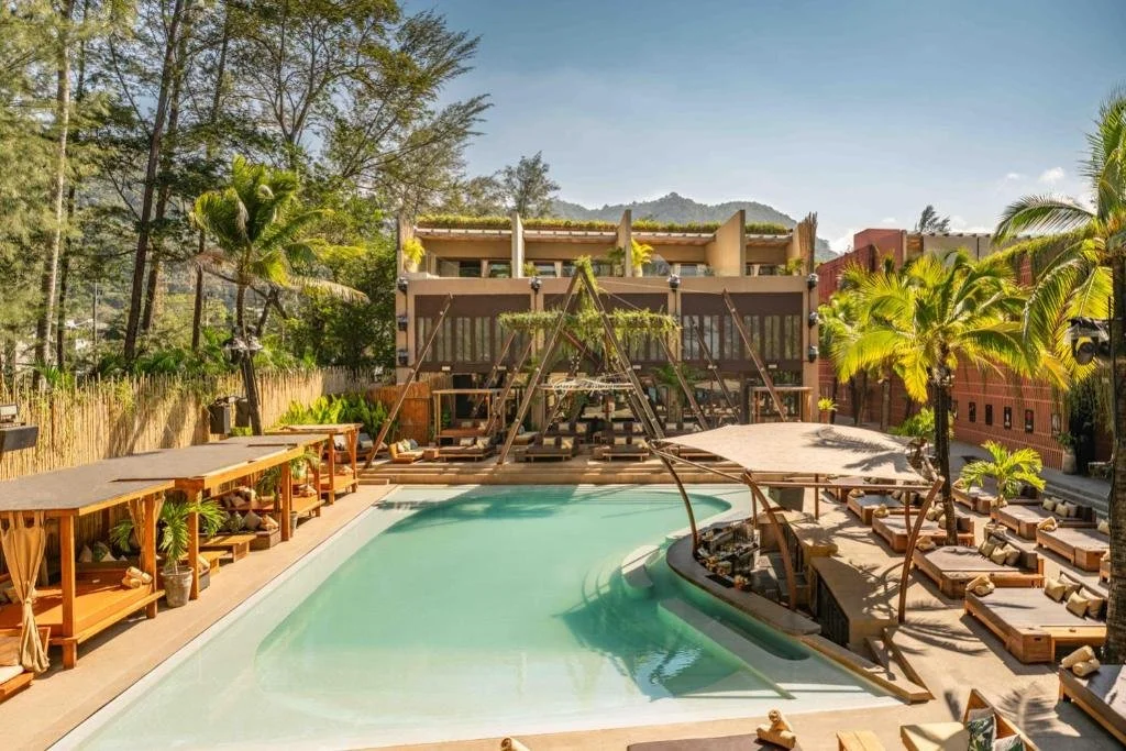 Luxury resort pool area surrounded by green palm trees and landscape, with lounge chairs and shaded cabanas under sunny sky.