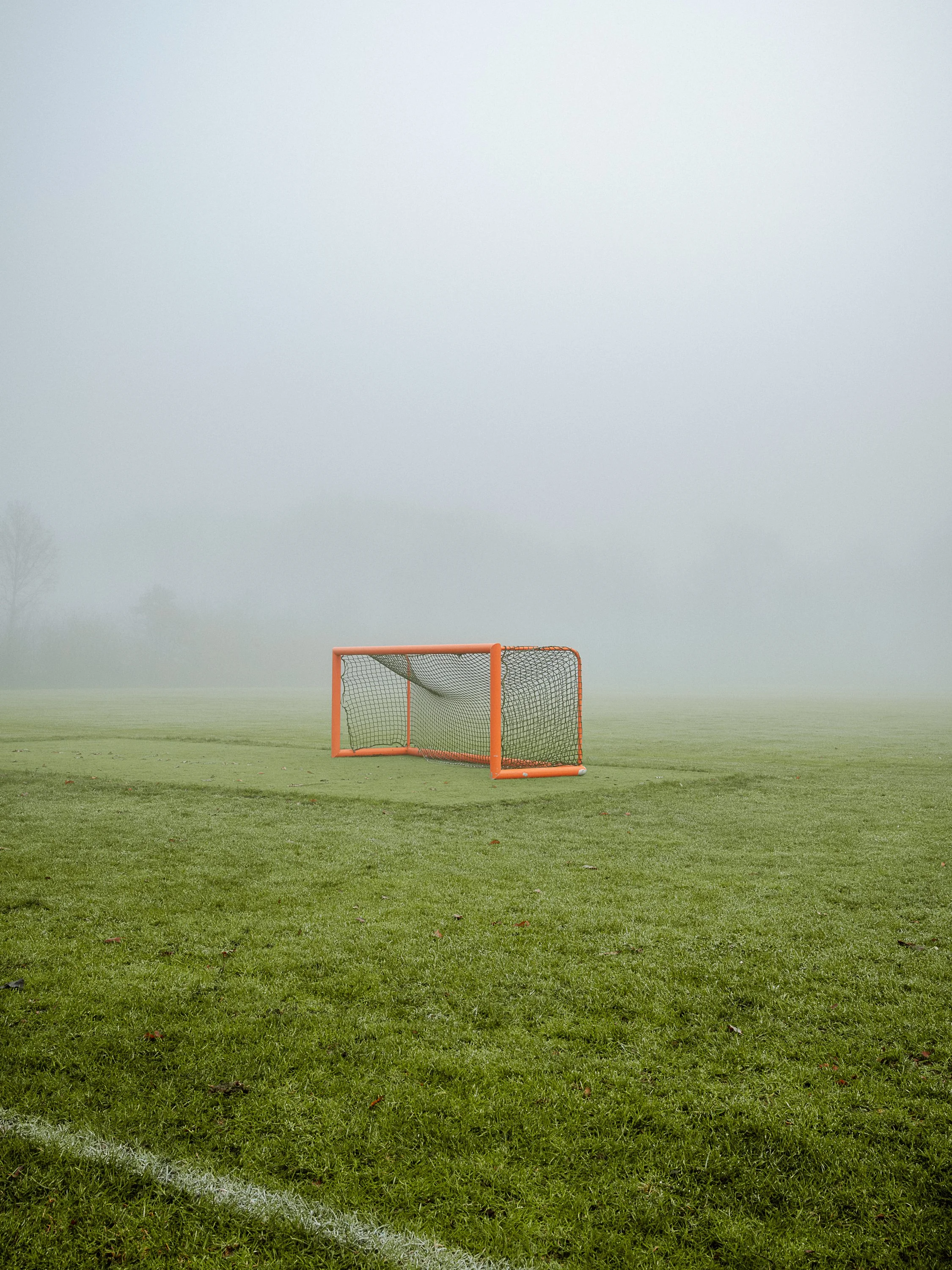An outdoor soccer field with a foggy atmosphere and a single orange goalpost in the foreground.