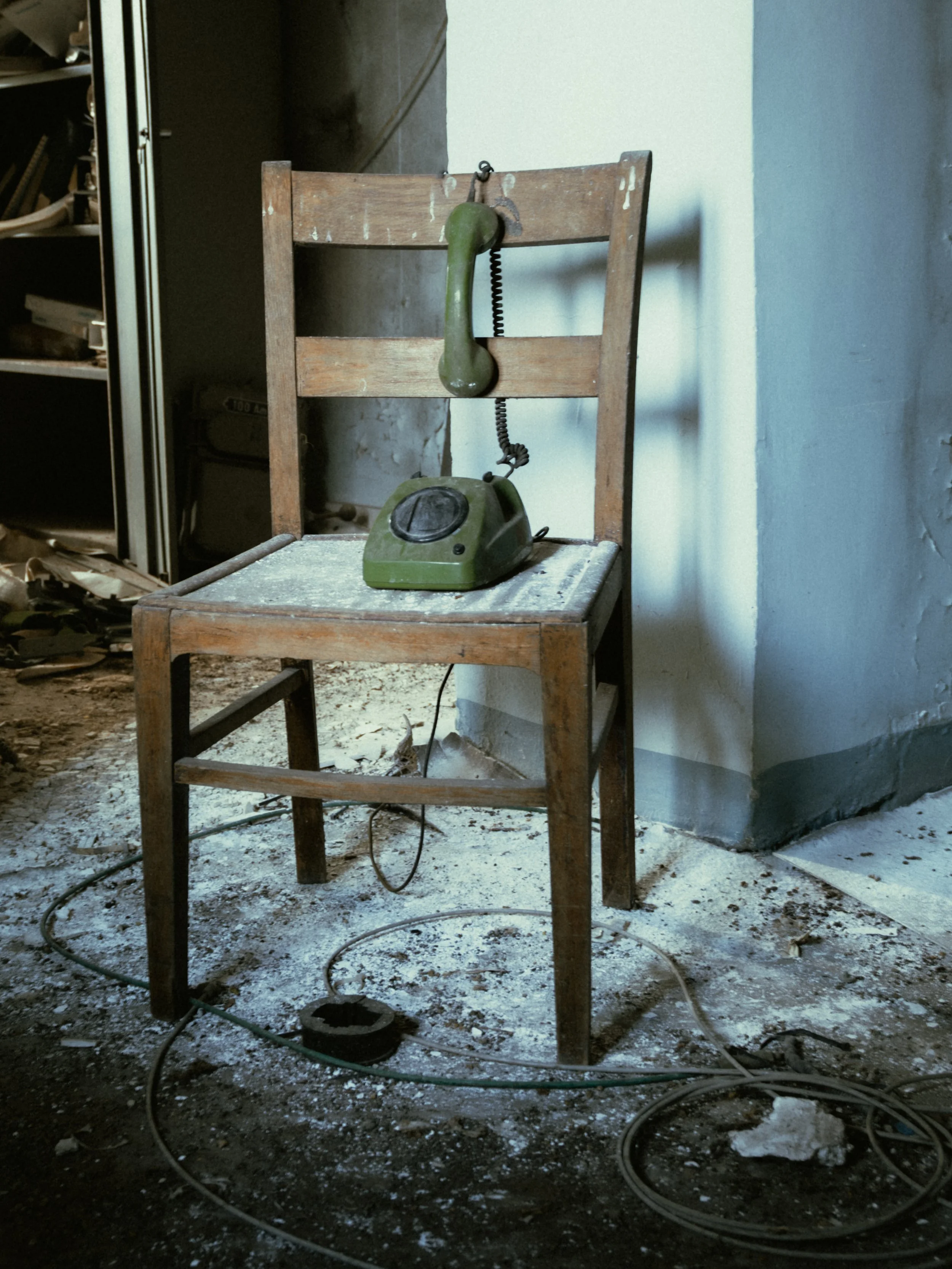 An old green rotary telephone resting on a small wooden table, with a string connecting the receiver to the base, in a dusty and dilapidated room.