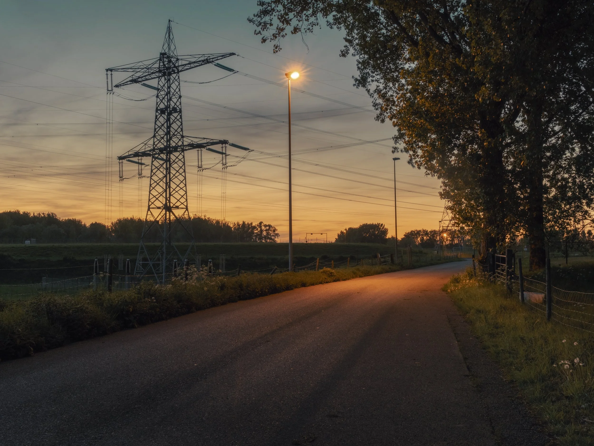 Sunset over a park with power lines, a streetlamp, and a tree on the right side.