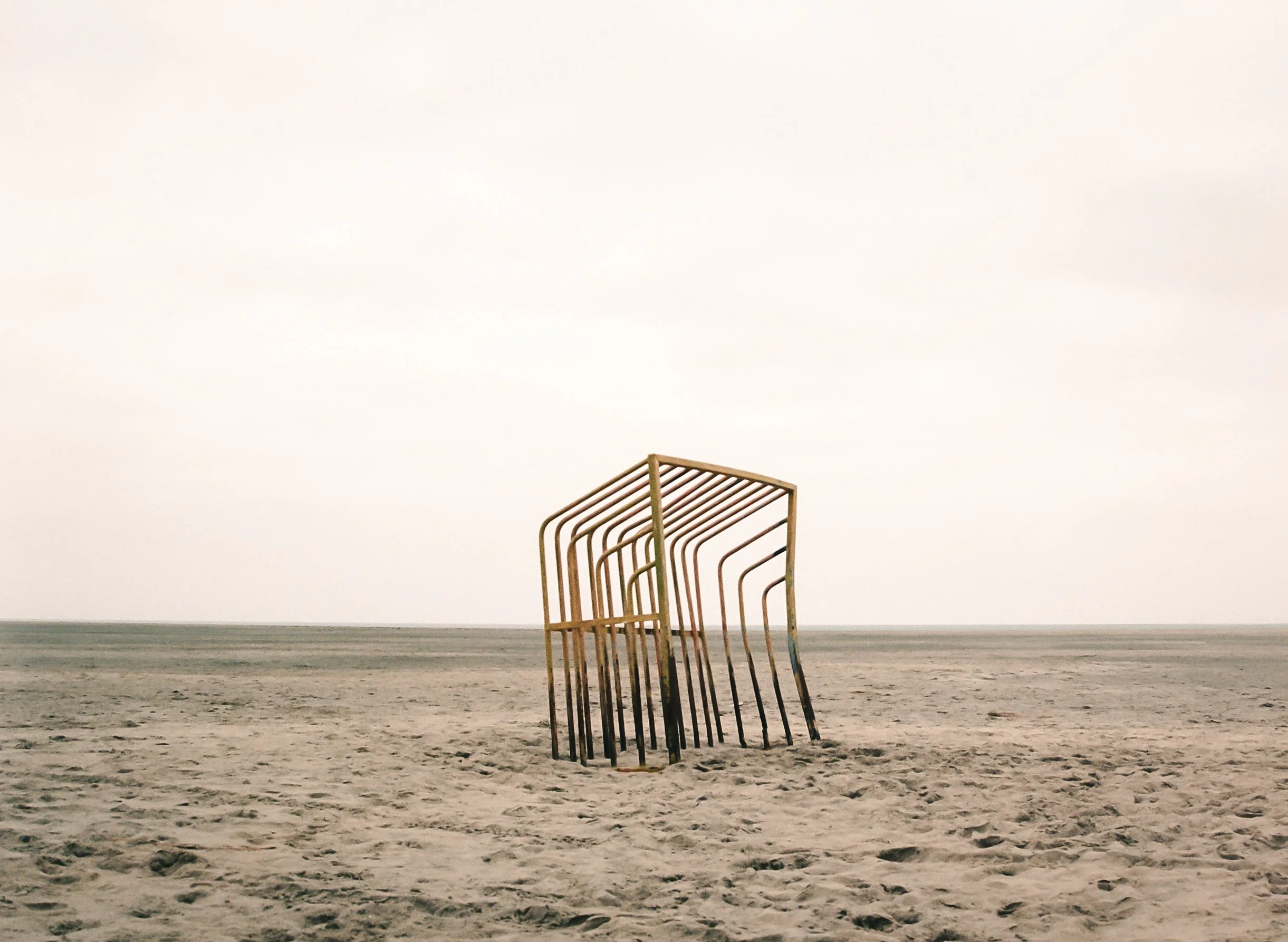 Stacked metal beach chairs on sand with a cloudy sky in the background.