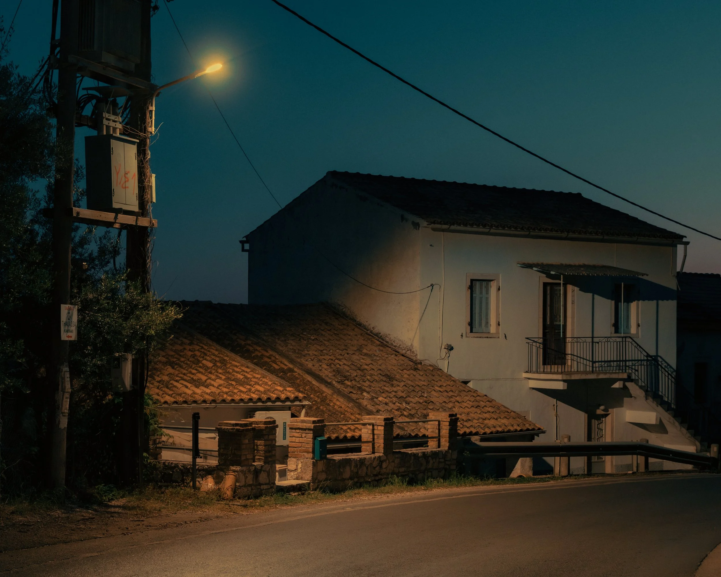 A quiet residential street at dusk with houses, a brick fence, and streetlights illuminating the scene.