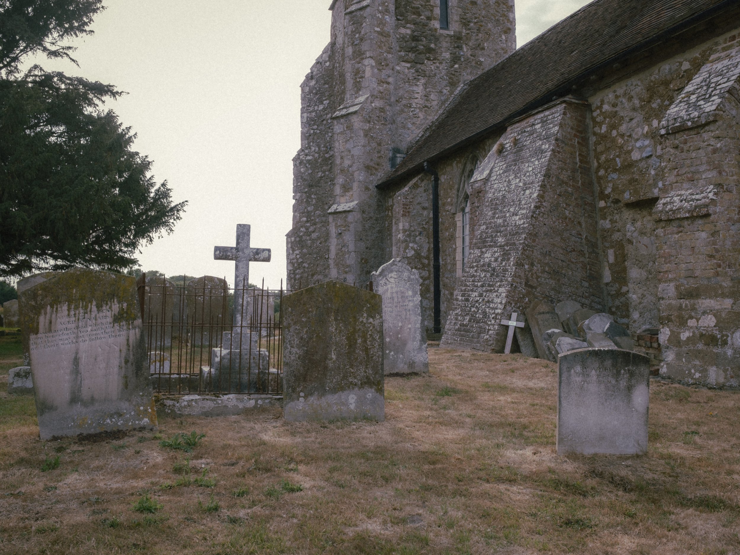 An old stone church with a tall tower and stained glass windows, surrounded by old gravestones and a black metal fence in a graveyard.