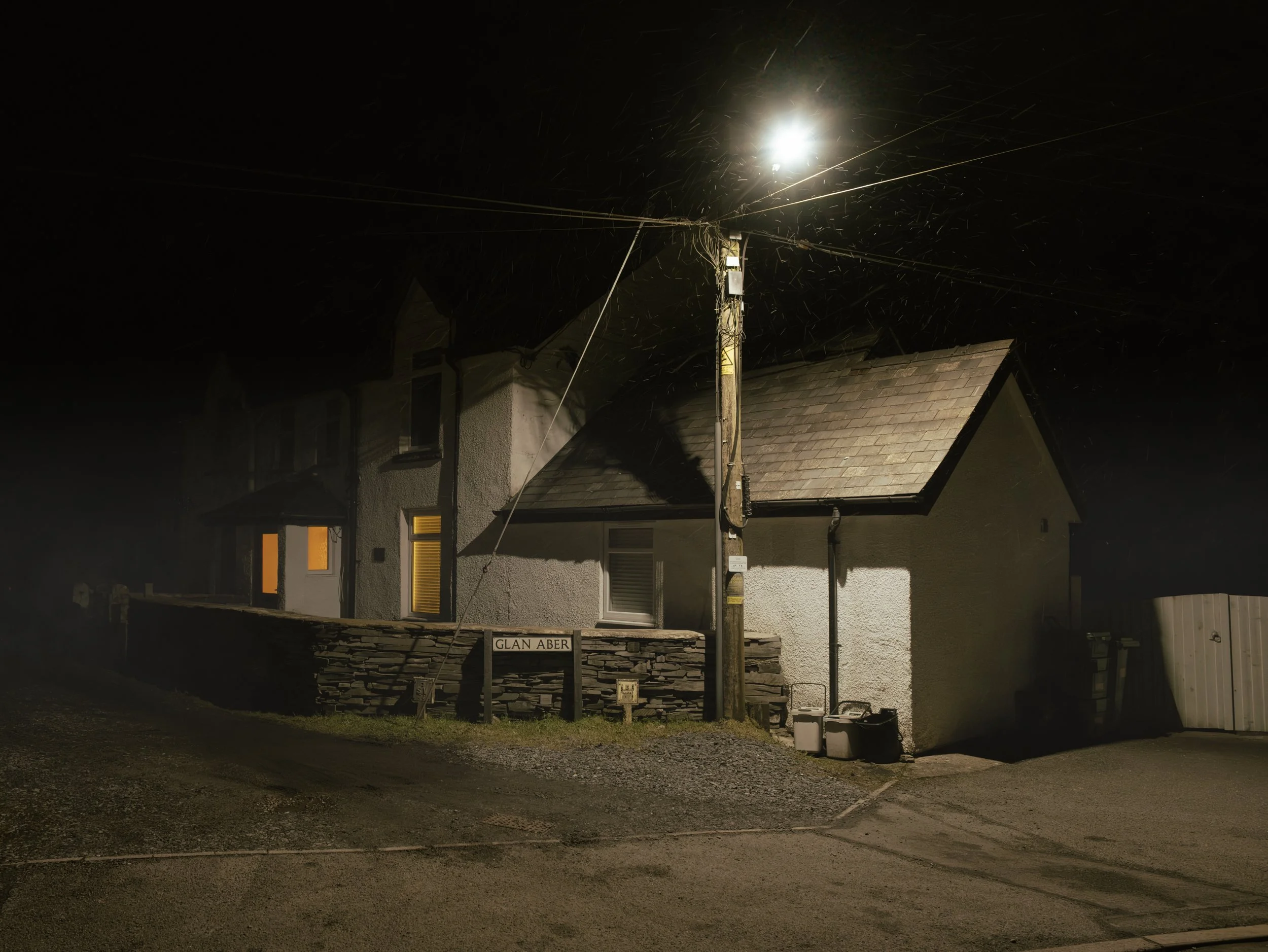 Nighttime view of a street with a house, streetlamp, and a street sign labeled "Glan Aber."