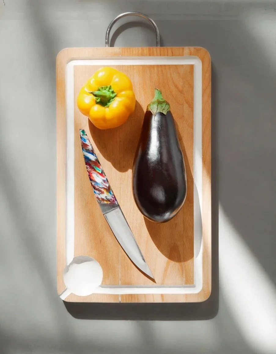 Un couteau de table le Demi-Lune placé sur une planche à découper en bois avec un poivron jaune, un aubergine noire.