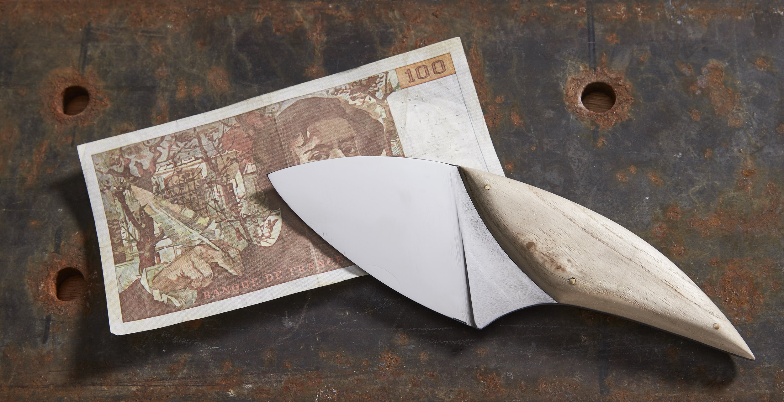 Un couteau de cuisine le Puck avec un billet de 100 francs Delacroix et un manche en bois de paulownia qui vient de l'arbre représenté sur le billet de 100 francs.