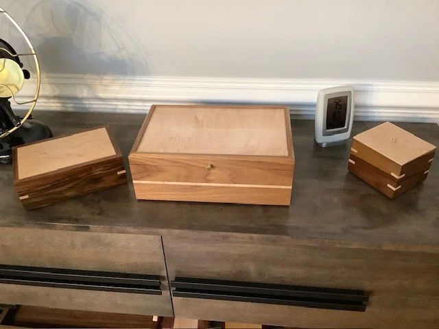 Wooden boxes with sliding lids on a dark wooden surface, with a digital clock and a vintage-style fan to the side.