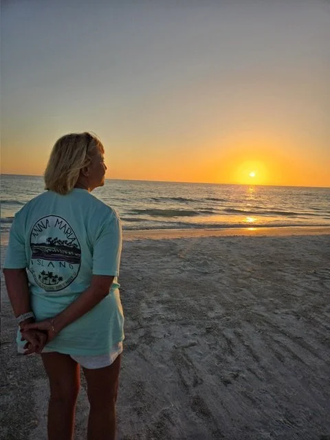 Woman standing on the beach watching the sunset over the ocean.